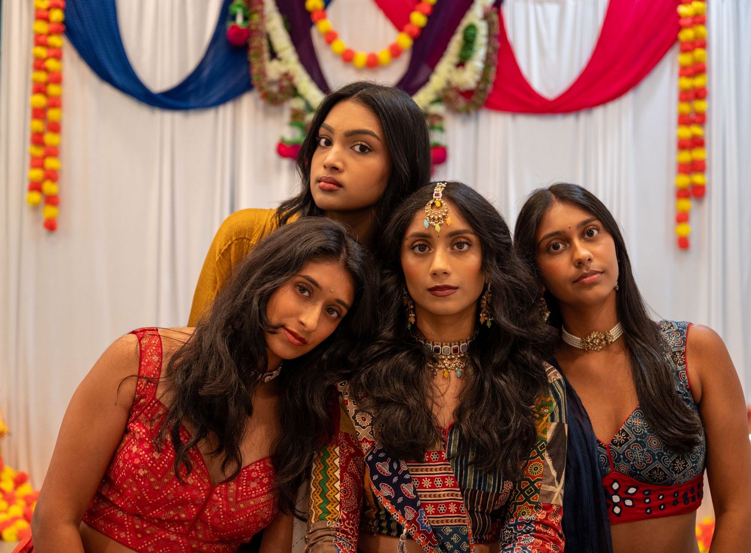 Women in traditional Indian clothing posing against backdrop with colorful festive decorations.