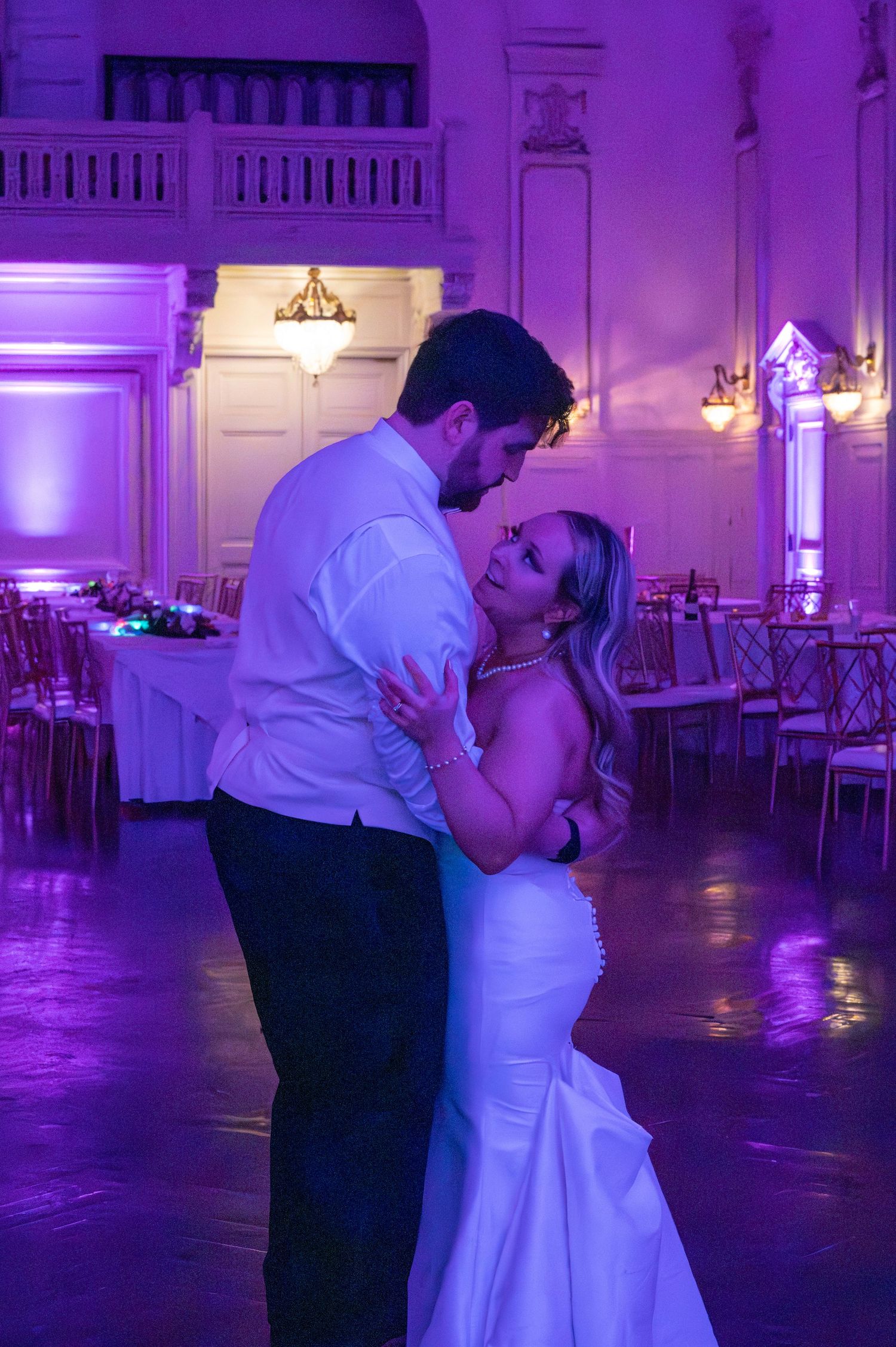 A couple shares their first dance in an elegant ballroom with purple uplighting and romantic ambiance.