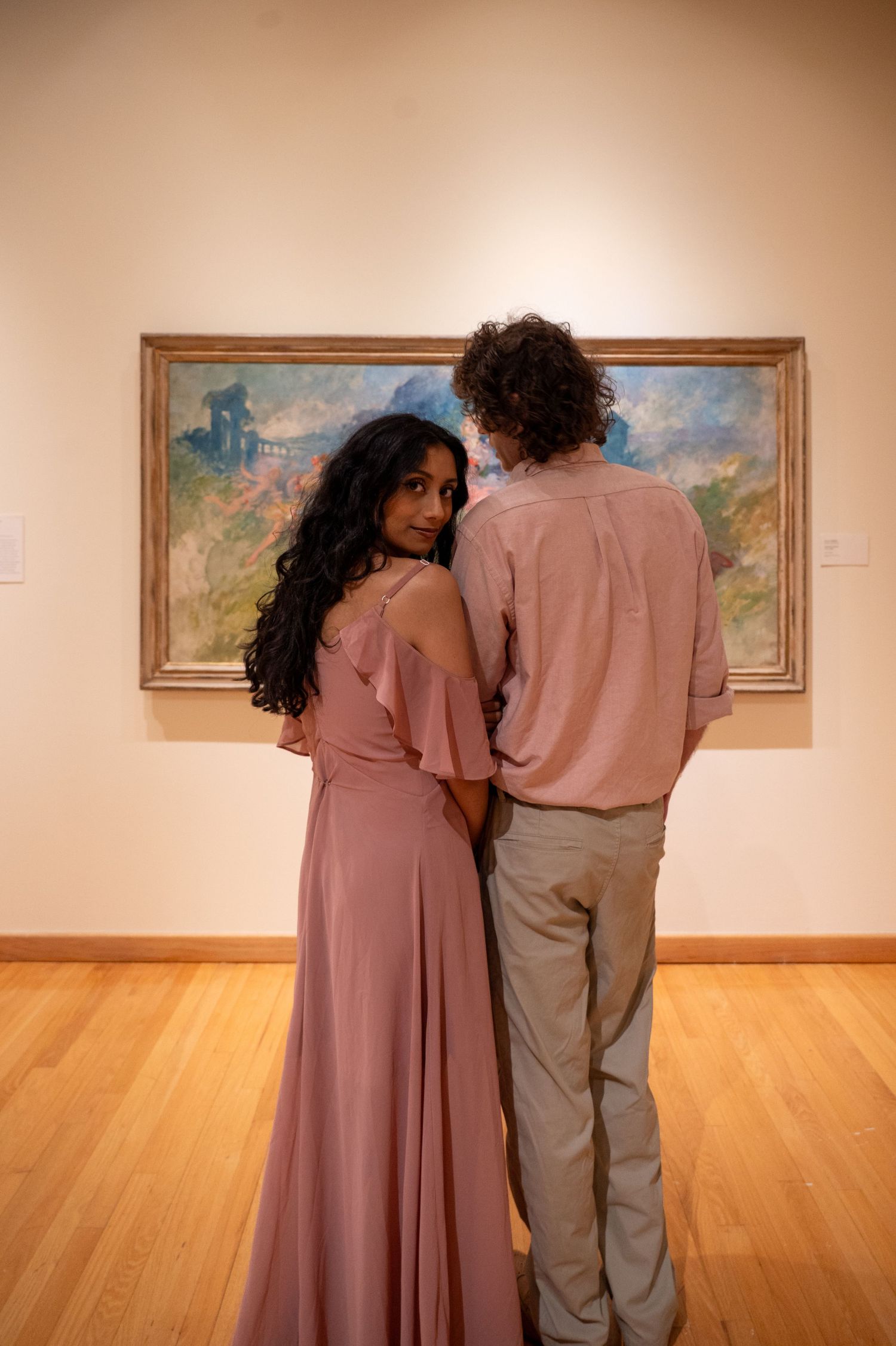 A couple admires artwork together in a museum gallery with hardwood floors.