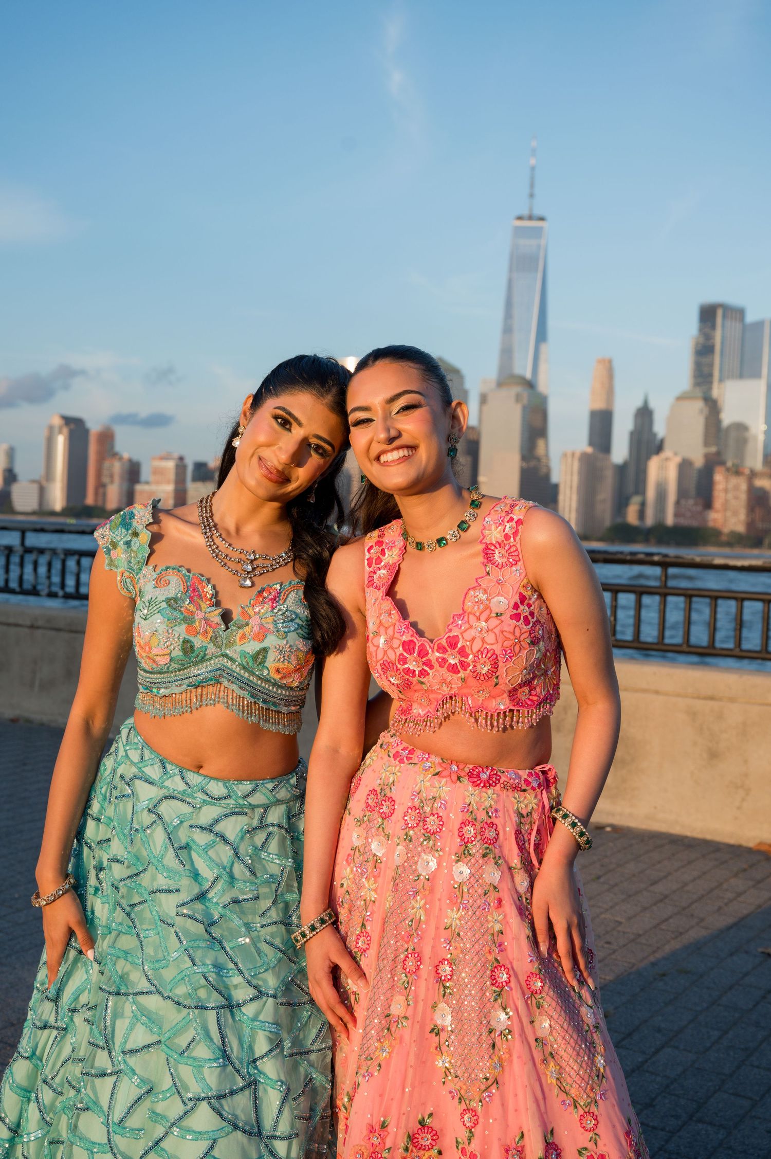 Two friends in floral dresses pose playfully against NYC skyline backdrop at sunset.