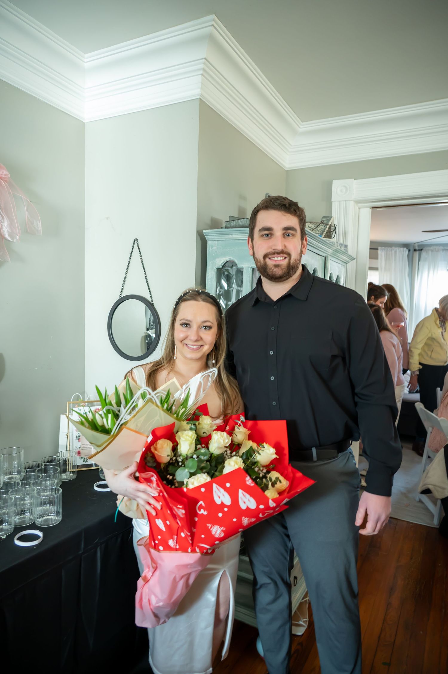 A bouquet of red and white roses wrapped in festive red paper being presented indoors.