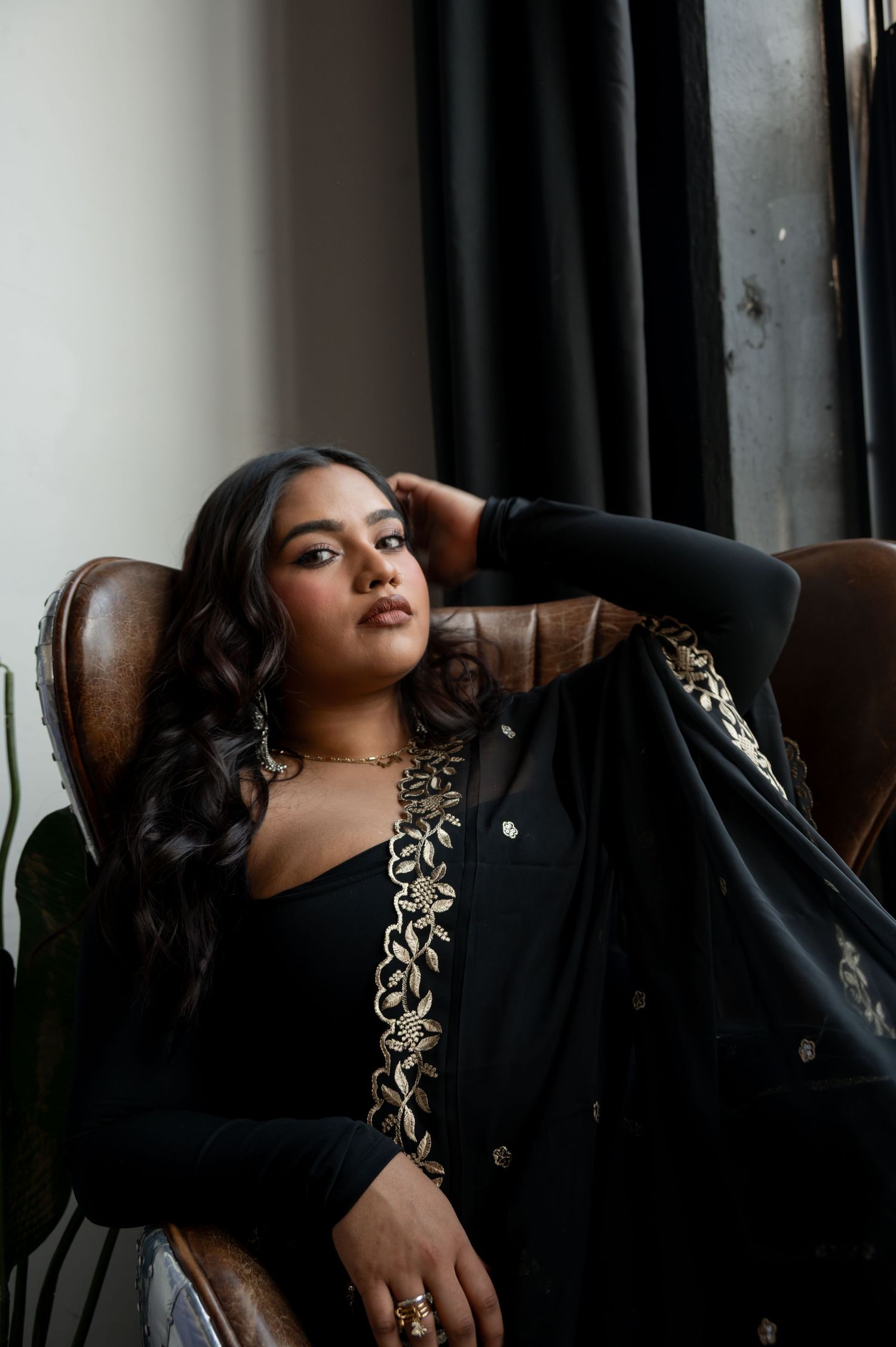 Elegant fashion portraits on leather chair featuring black dress with gold embellishments.