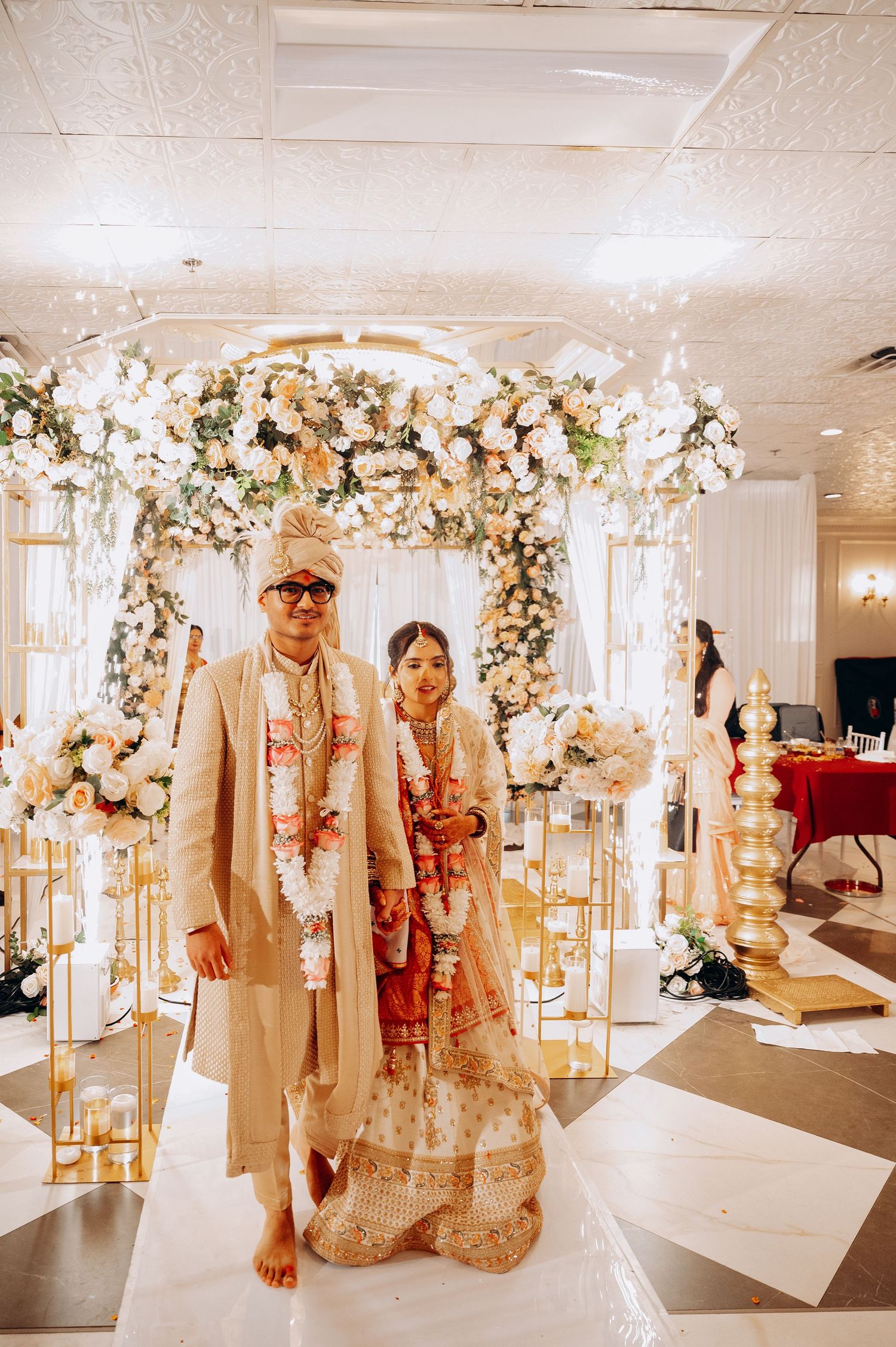 Wedding ceremony setup with white floral arches and decorations in an indoor venue.
