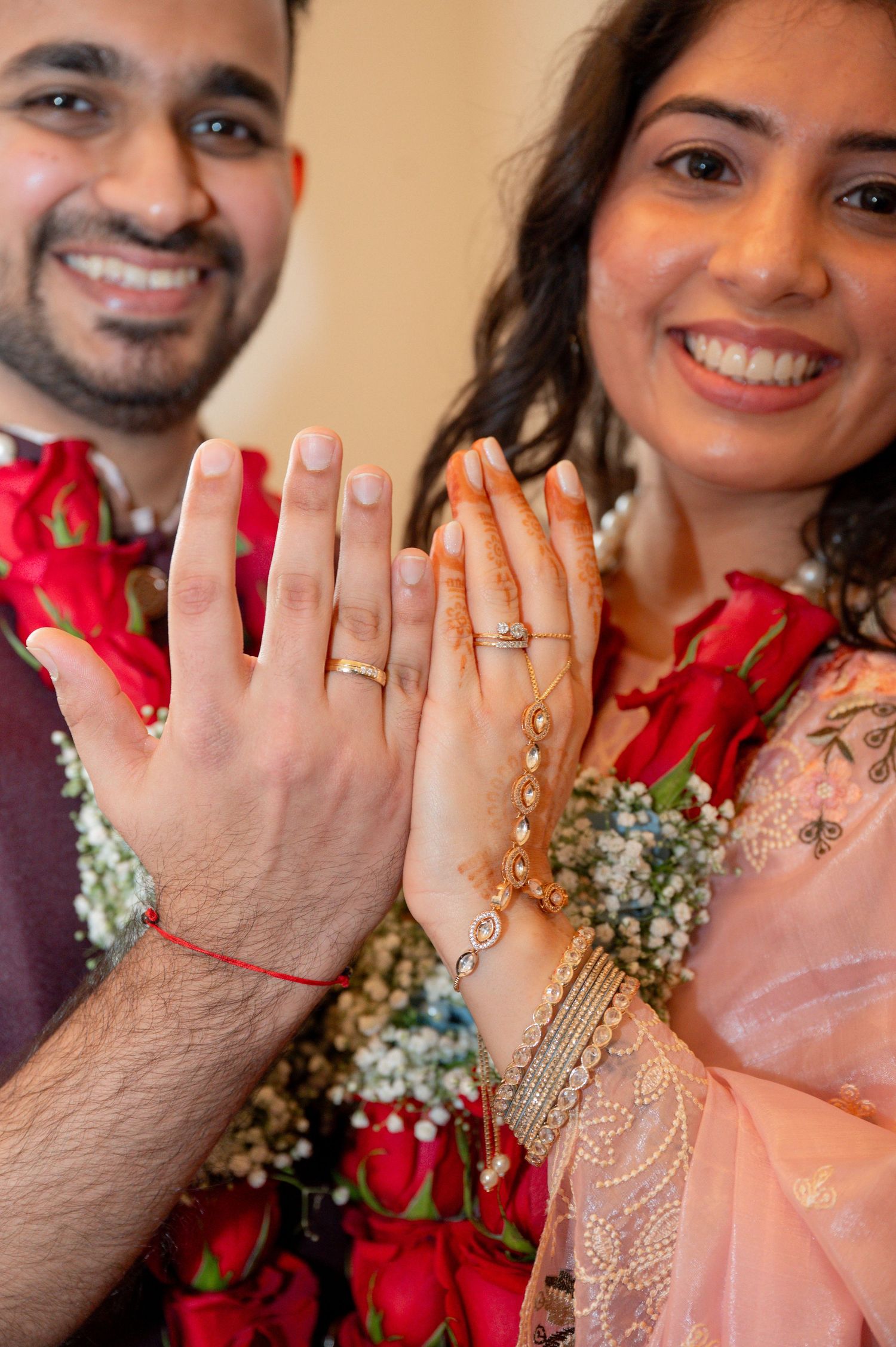 A series of hands displaying wedding rings with red rose petals and baby's breath flowers in the background.