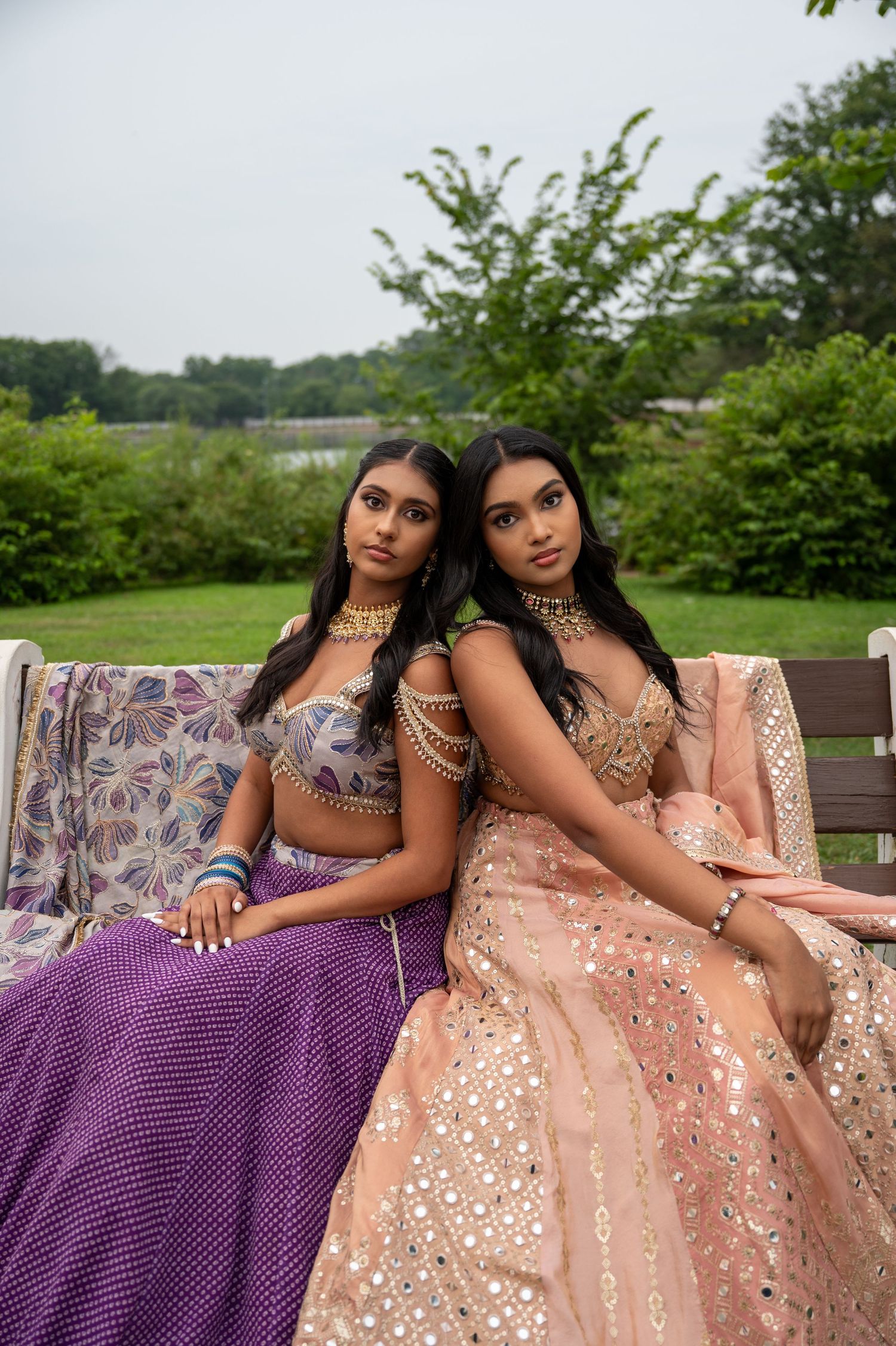 Two models in coordinating formal wear pose together on outdoor bench.