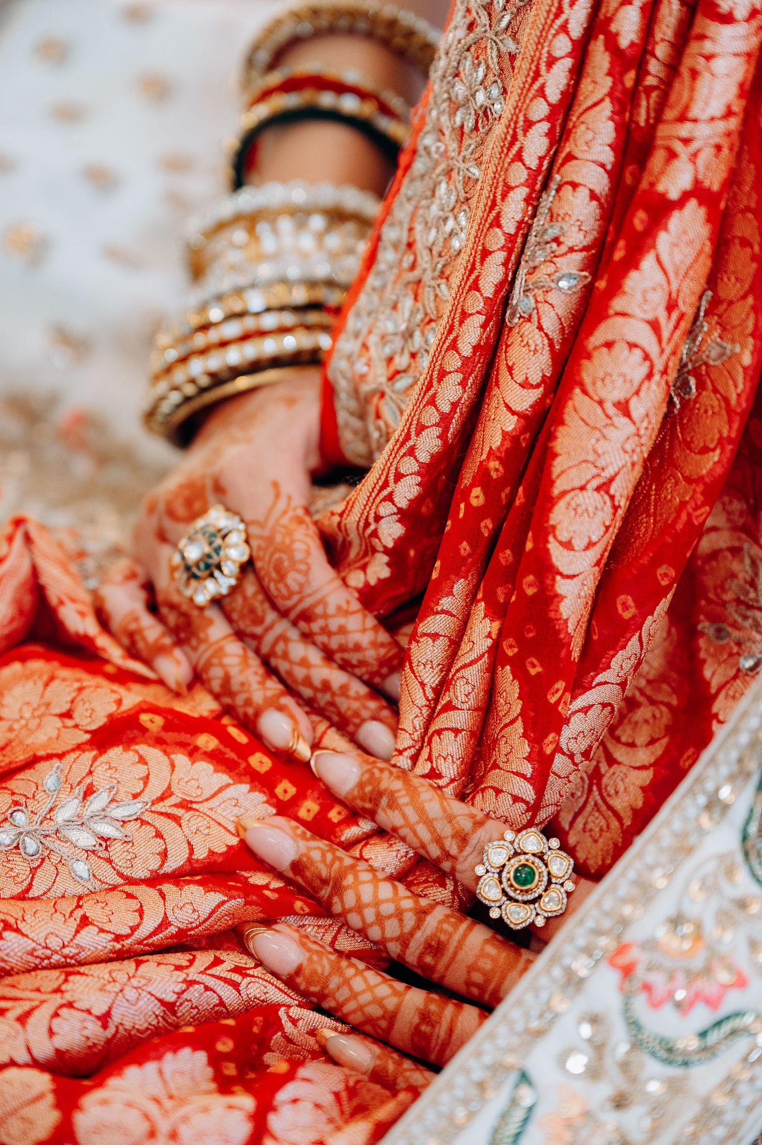 Close-up of hands adorned with traditional henna designs and jewelry on red fabric background.