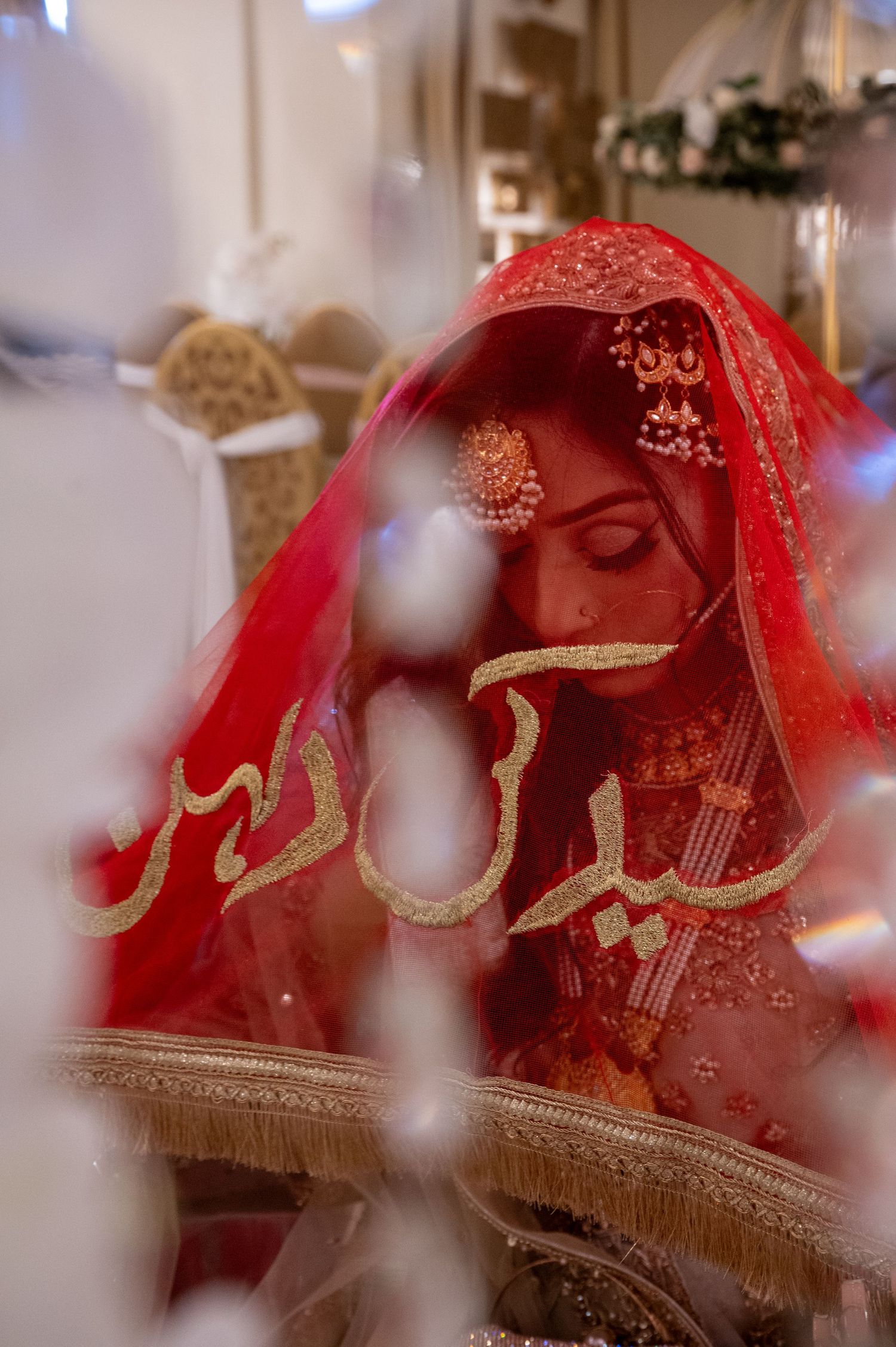Artistic wedding photo through sheer fabric with red and gold traditional details.