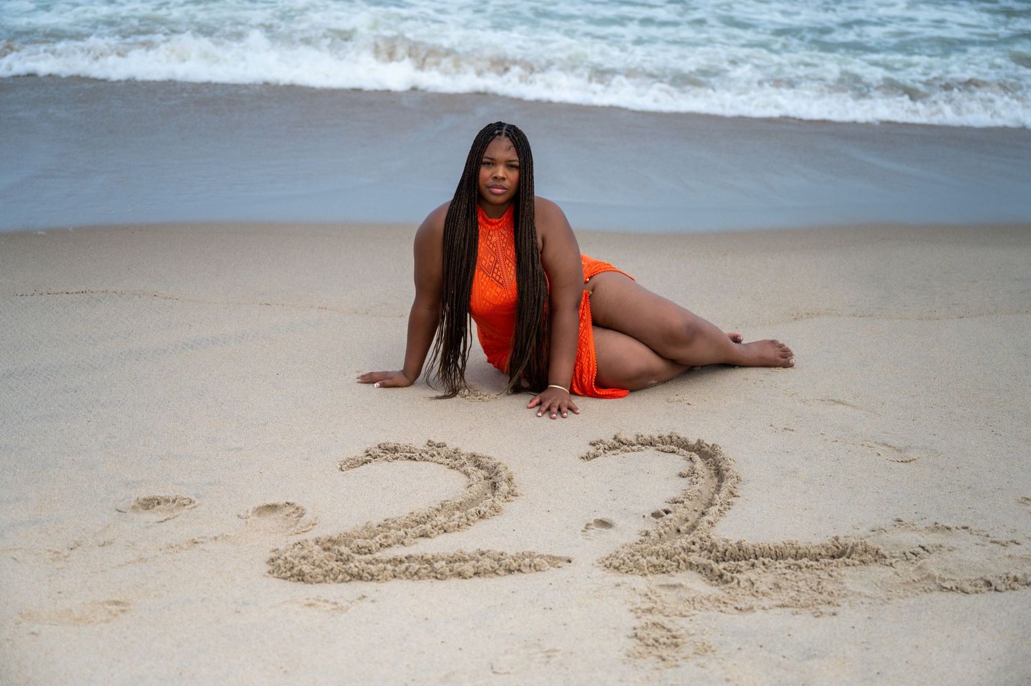 Person in orange swimwear relaxes on beach near waves.
