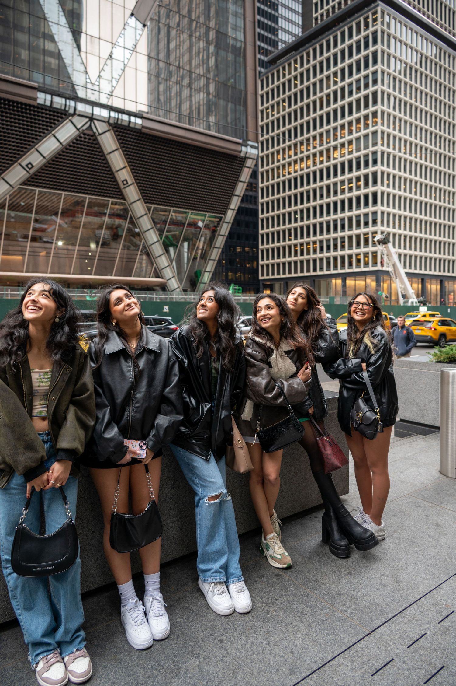 Friends posing together on city sidewalk with modern skyscrapers in background.