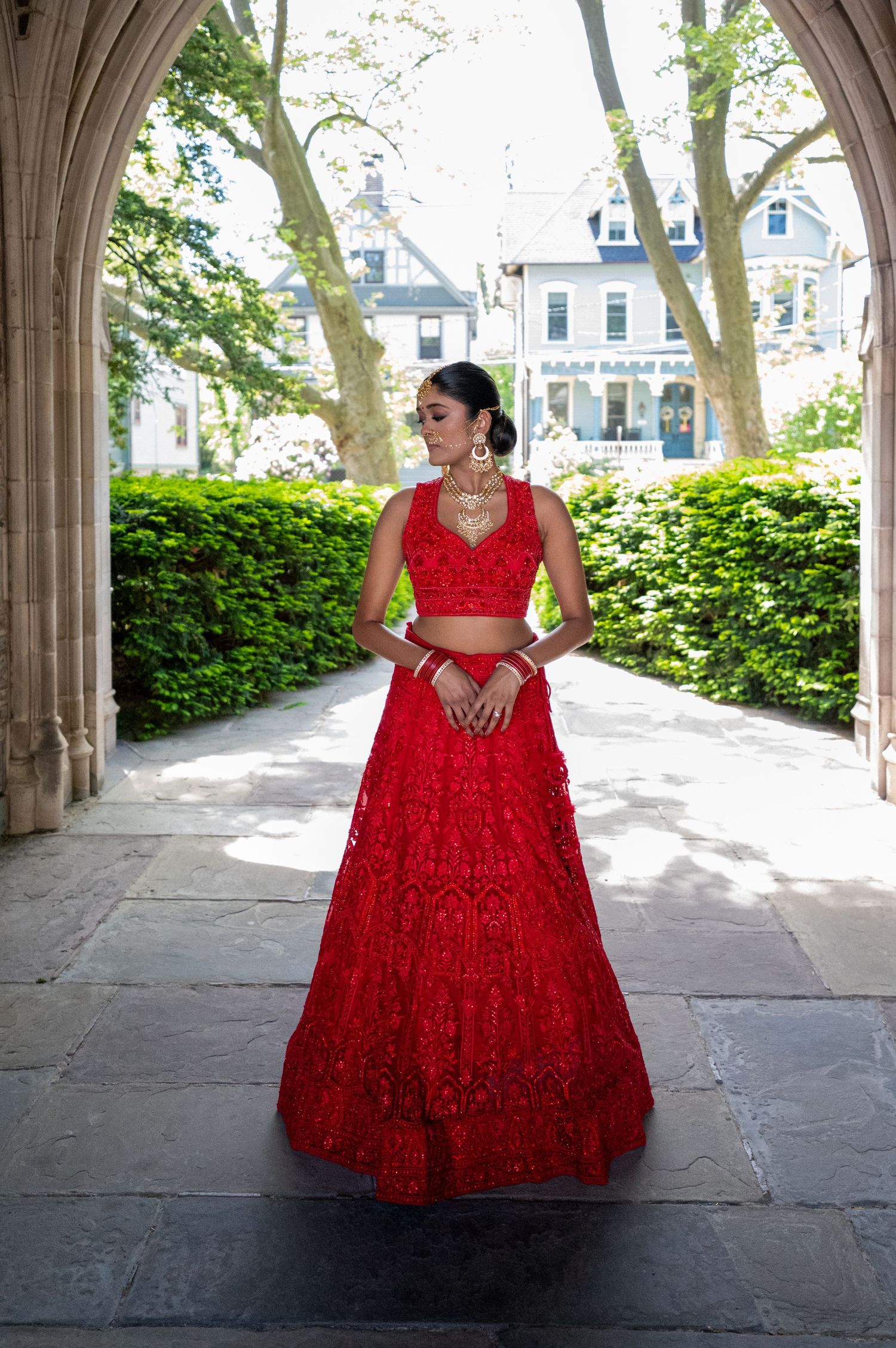 Full-length portrait under stone archway wearing a red sequined ball gown.