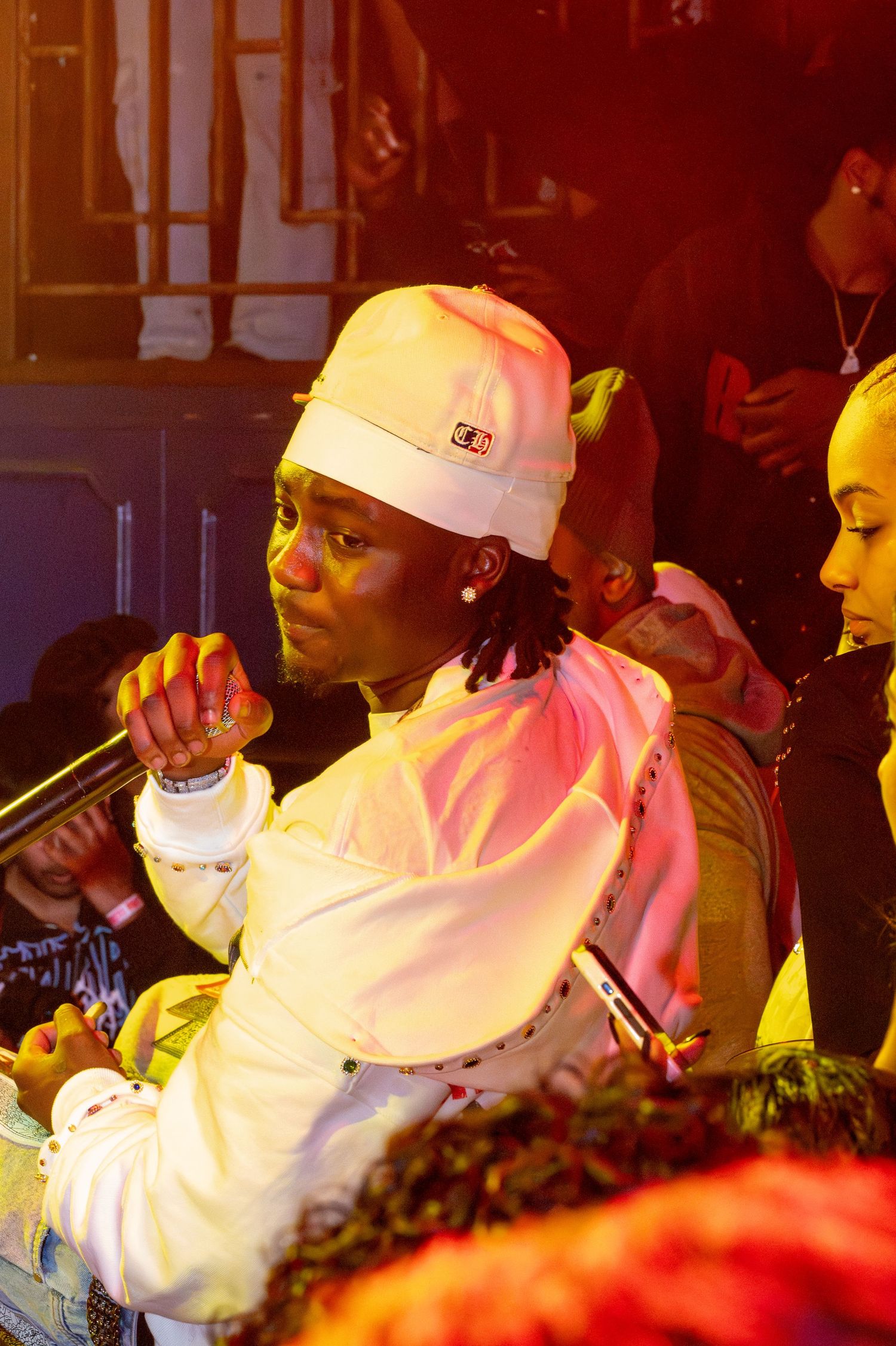 Performer in white attire and baseball cap holds microphone during nightclub show.