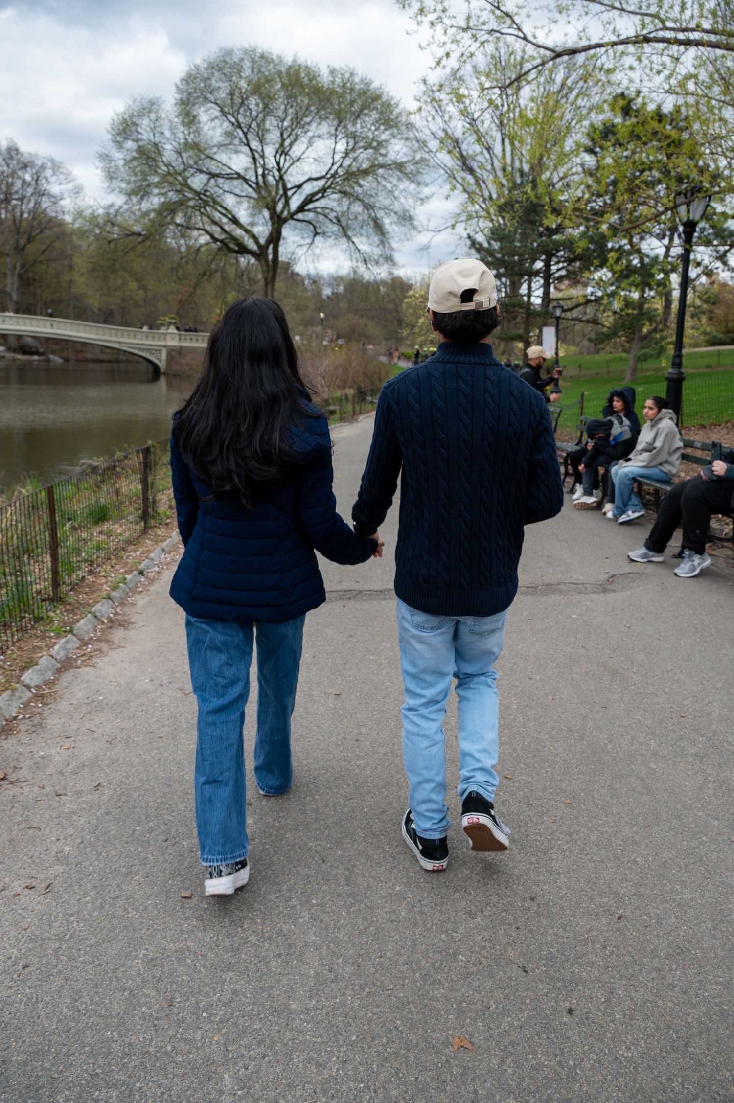 A couple walking hand in hand along a park path on a cloudy day.