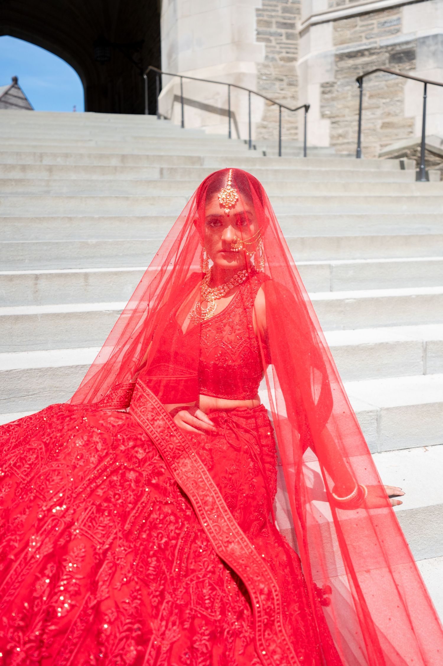 A flowing red gown with sparkles and tulle veil photographed on stone steps.