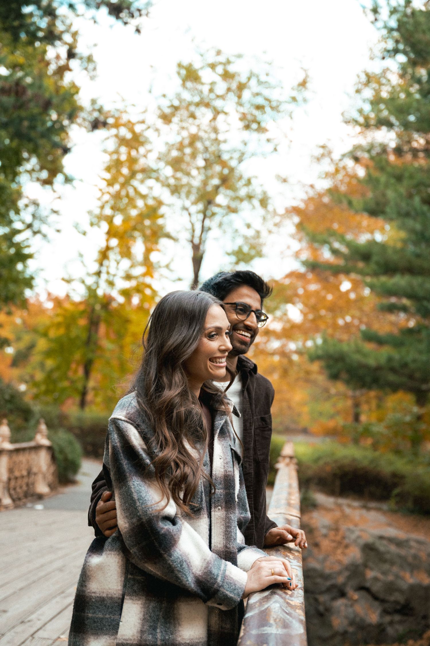 A couple enjoying autumn weather while standing on a rustic bridge surrounded by fall foliage.