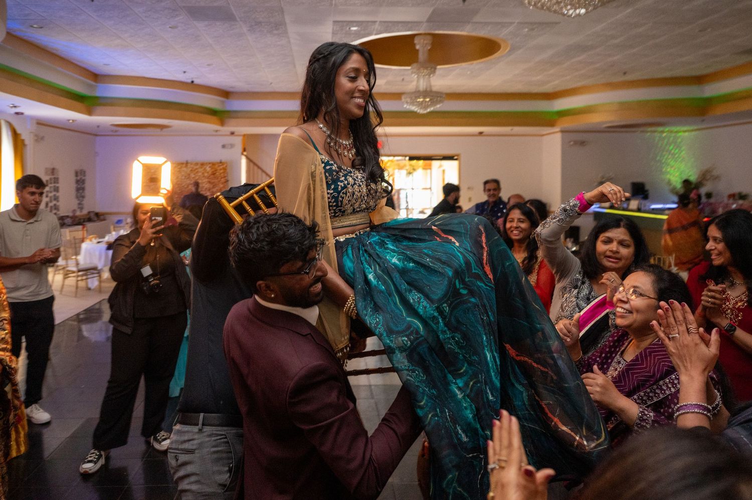 Celebrants lifting and dancing with guests during a festive indoor party.