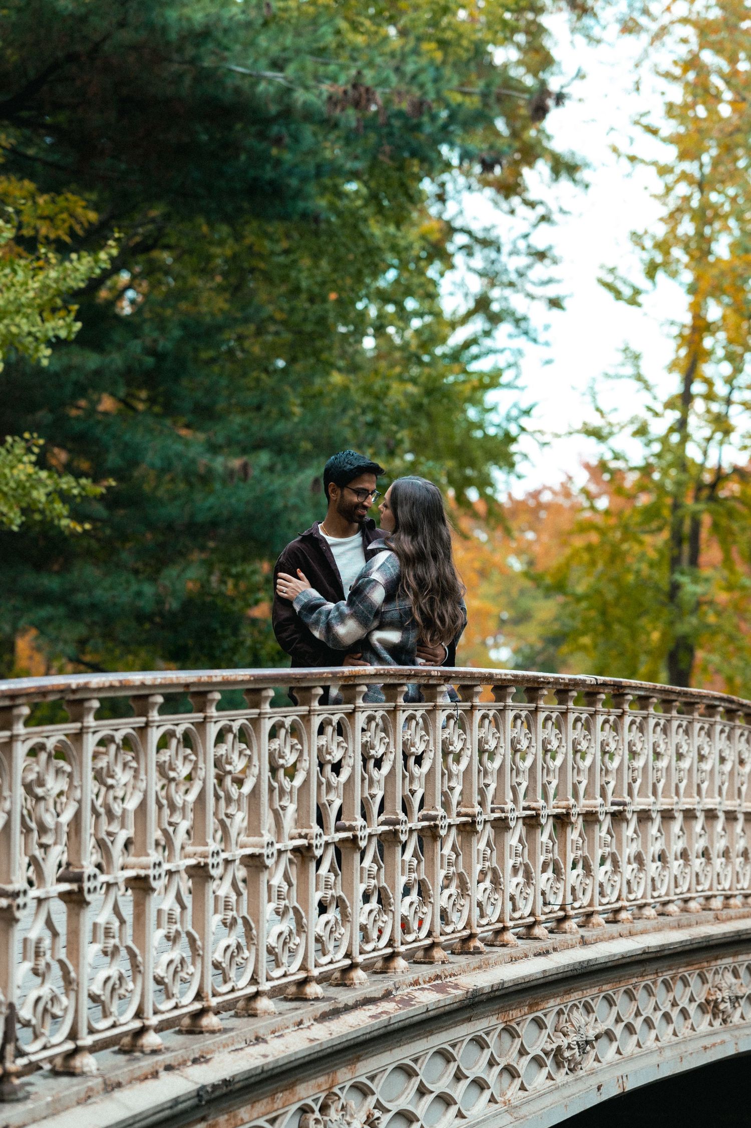 A couple embraces on an ornate bridge surrounded by autumn foliage.