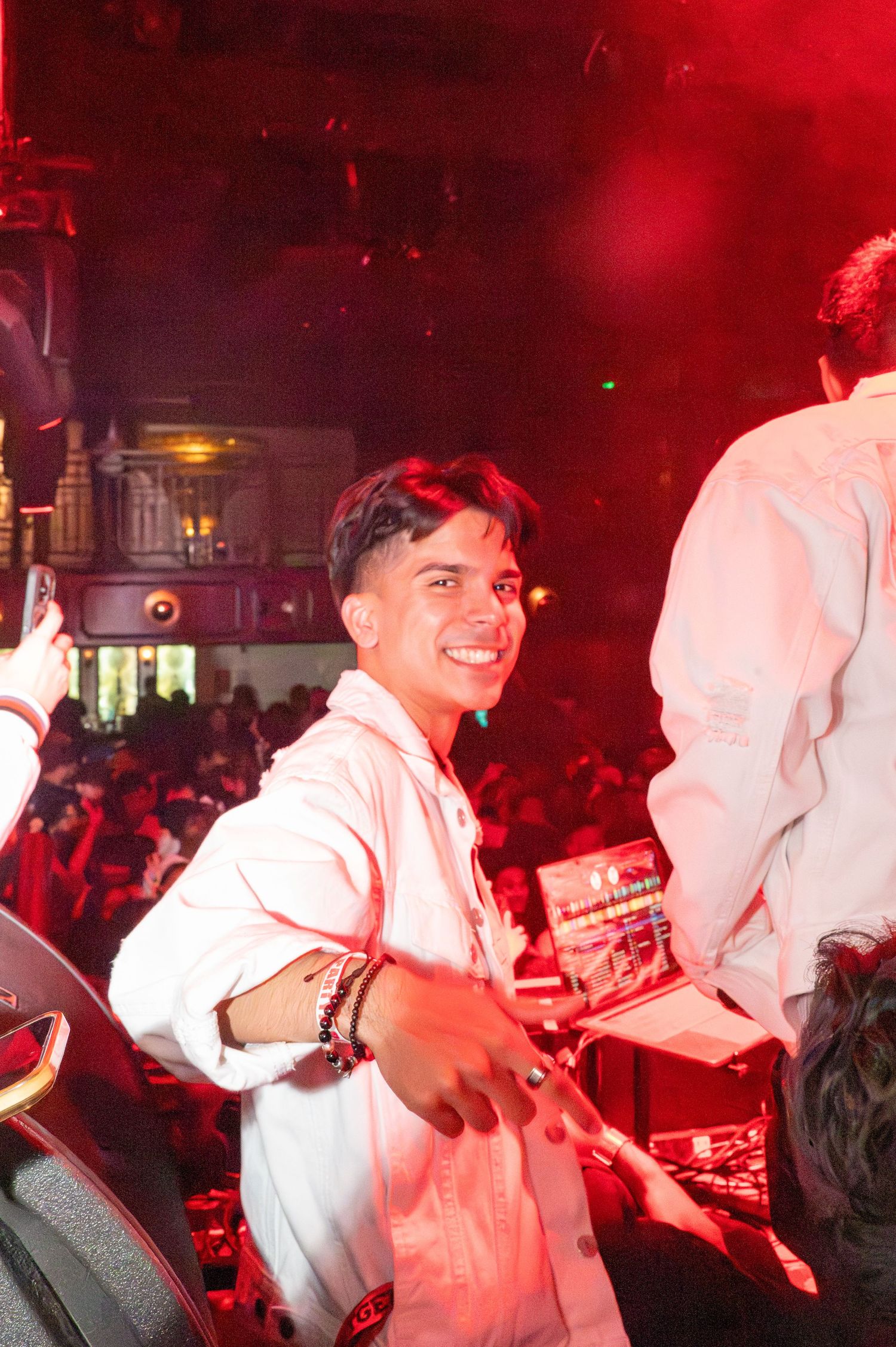 A DJ performs at a nightclub under dramatic red lighting while entertaining the energetic crowd.