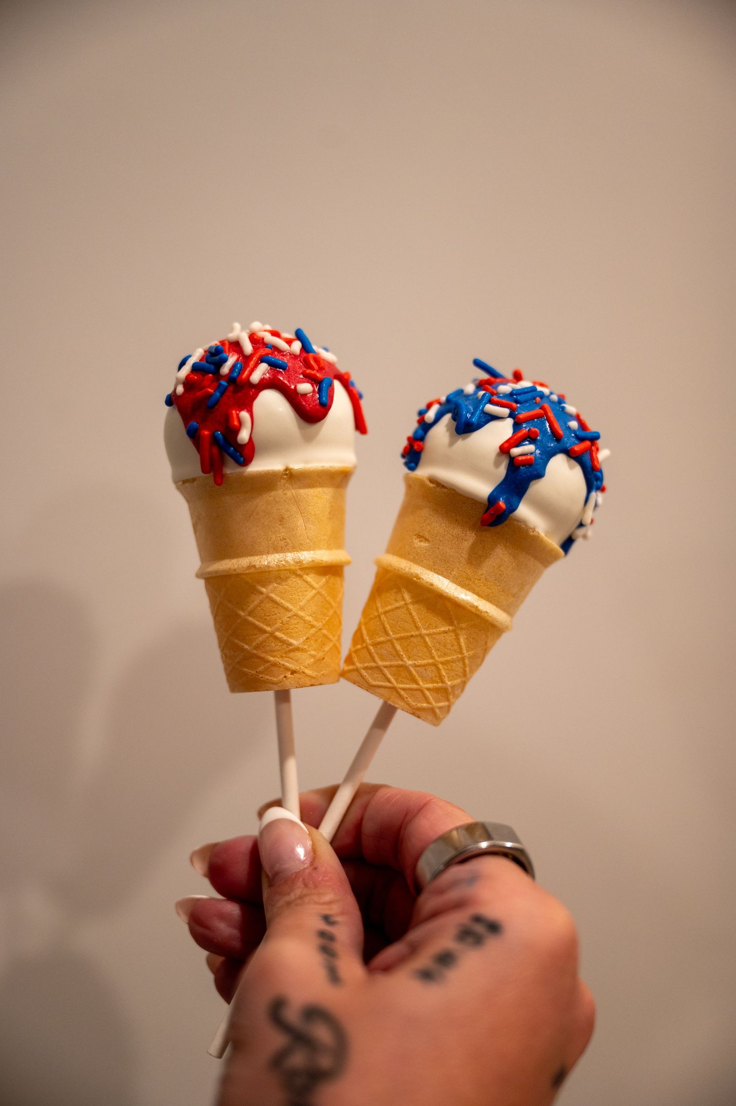 Two ice cream cones topped with red and blue sprinkles held against a neutral background.