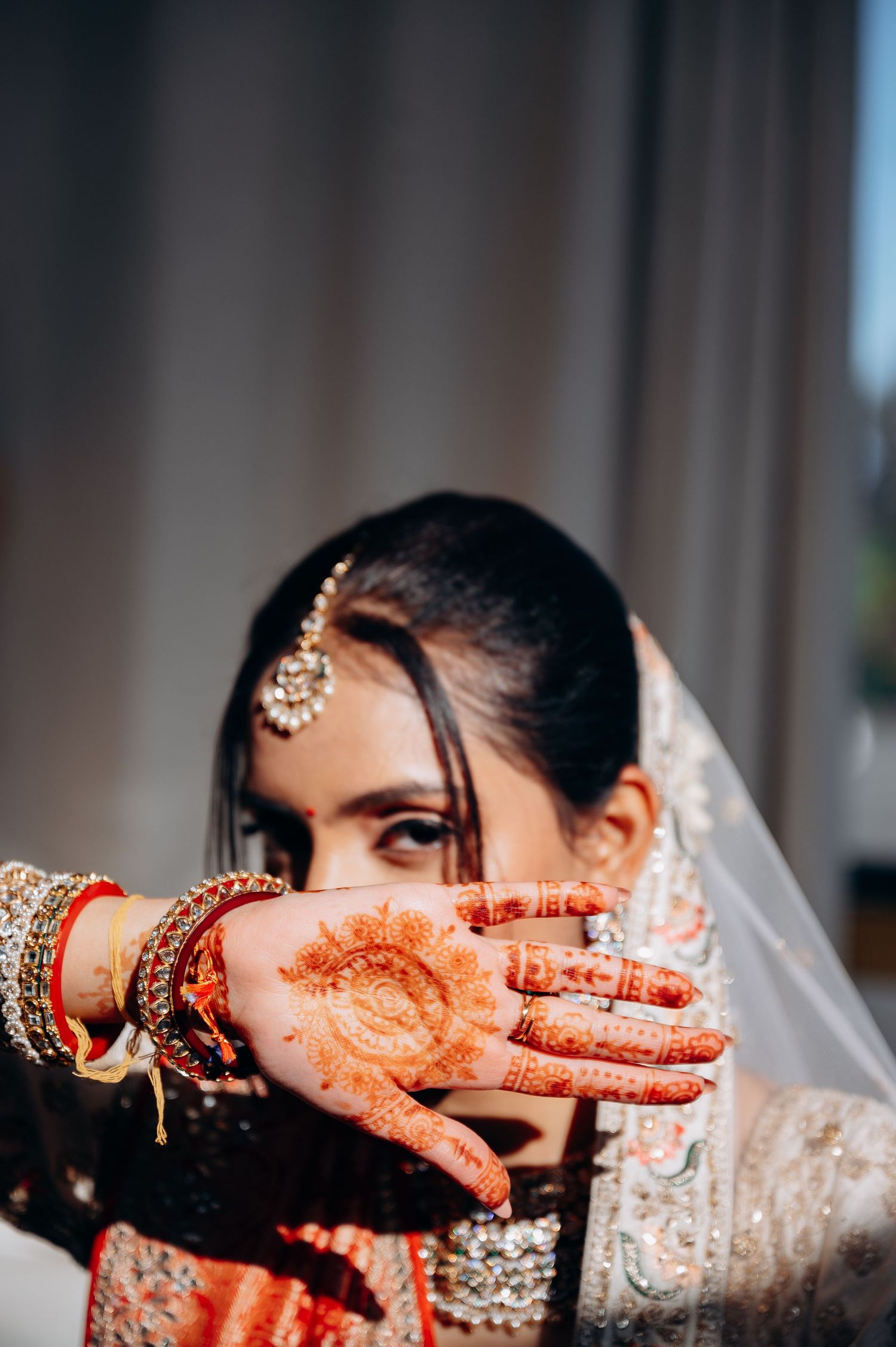 Artistic bridal portrait showing henna-decorated hands and traditional wedding jewelry.