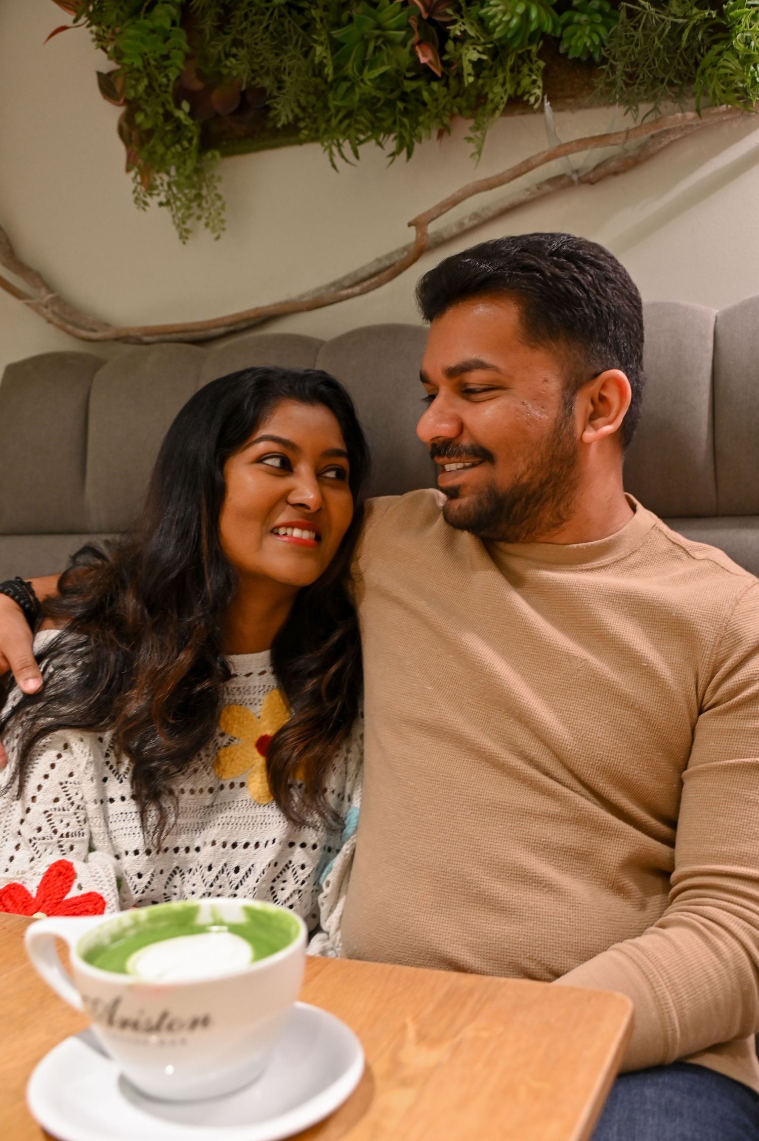 Cozy couple sharing intimate moments on a sofa with coffee and greenery in the background.