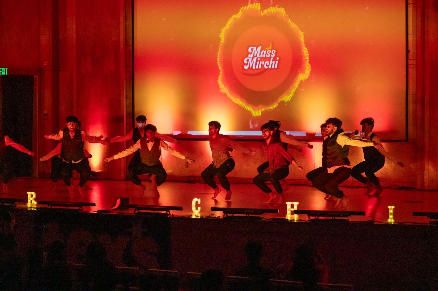 Dancers perform in dramatic red lighting with glowing effects on a dimly lit stage.