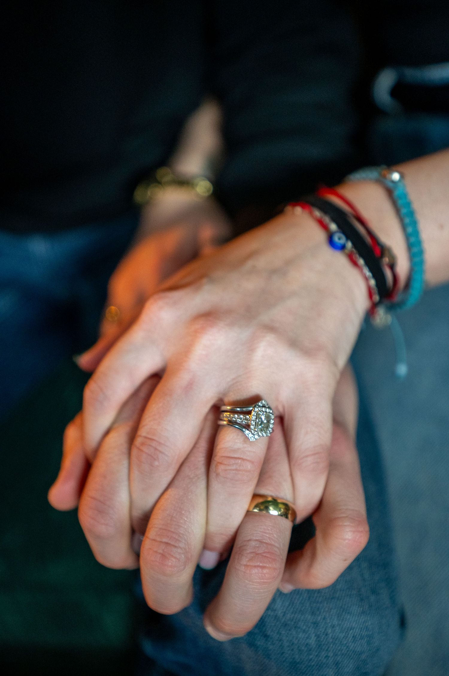 Close-up of intertwined hands wearing engagement ring and colorful friendship bracelets.