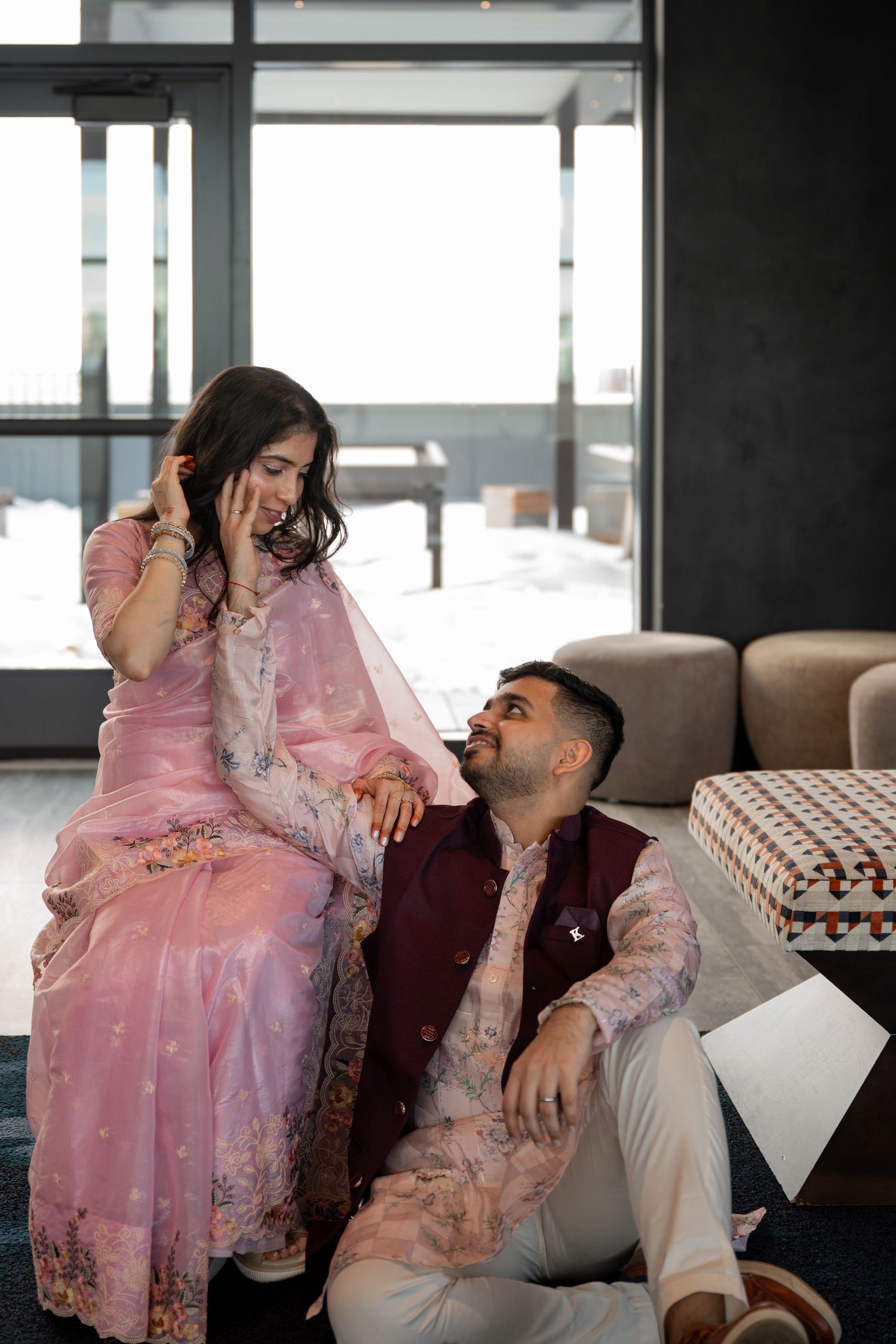 A couple in romantic poses on a couch, with the woman wearing a pink embellished dress.