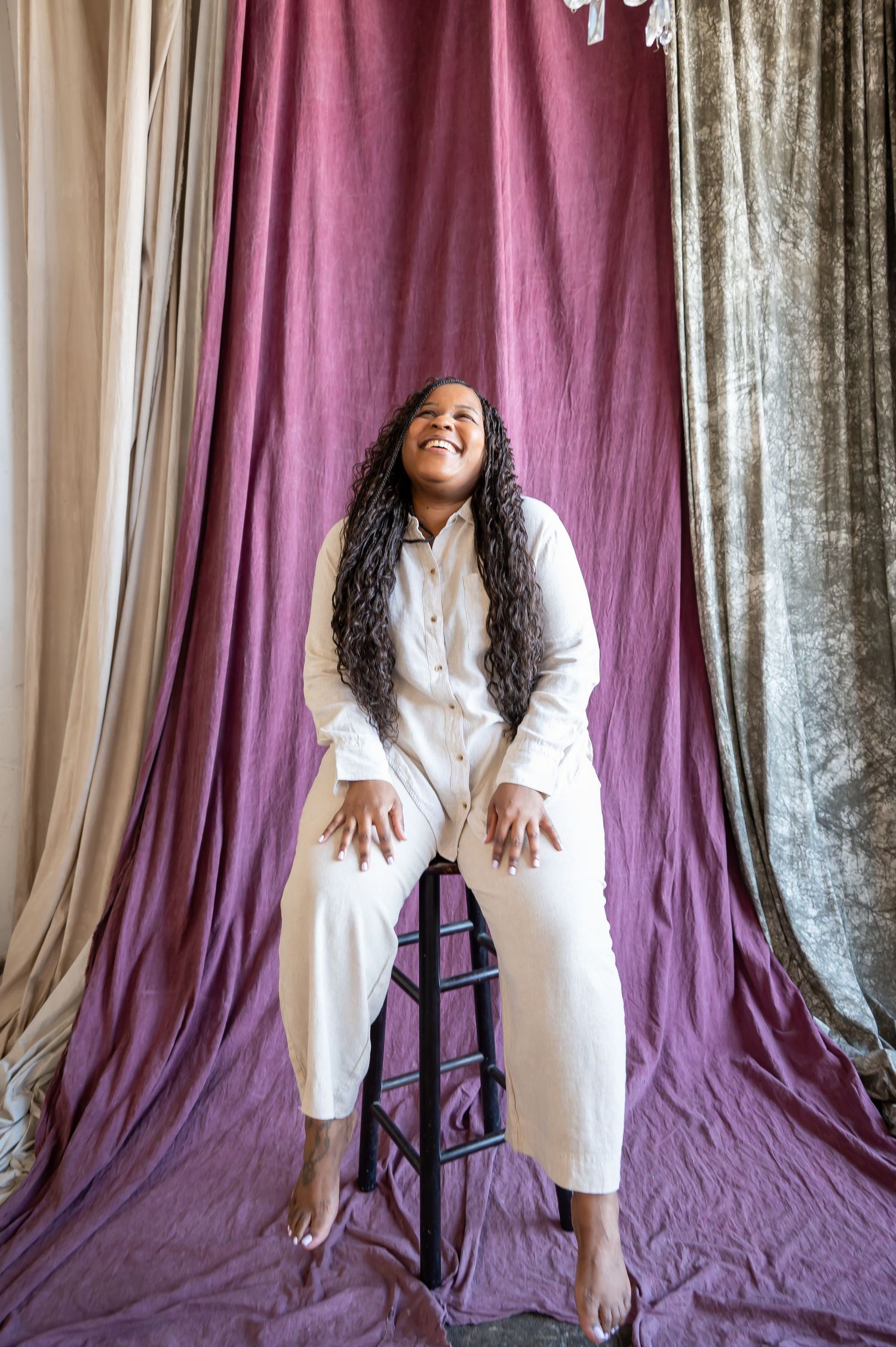 Person in white dress poses against purple and silver curtain backdrop.