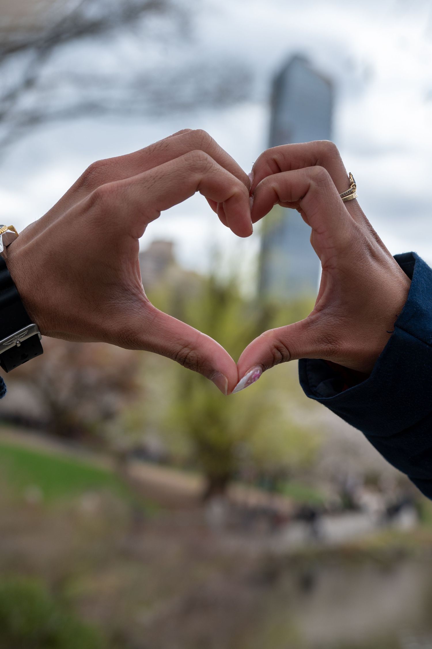 Two hands form a heart shape against a blurred city backdrop.