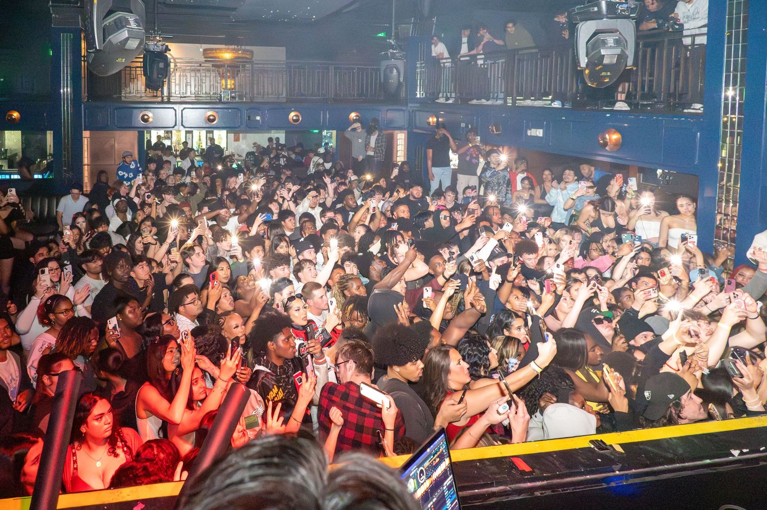 Large crowd of enthusiastic fans at a packed nightclub event with raised hands and phones.