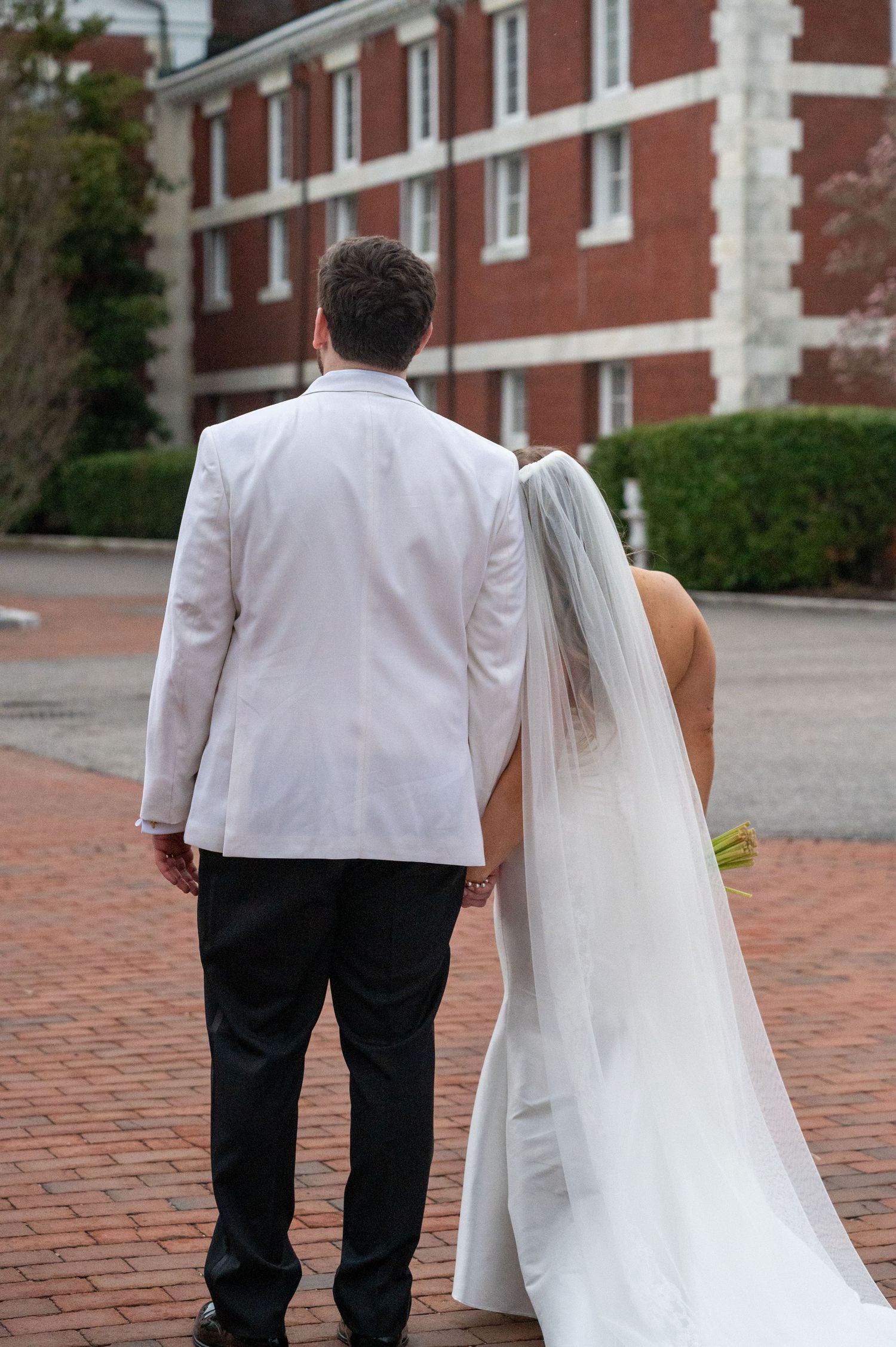 A couple walks together on a brick pathway outside a stately red brick building.