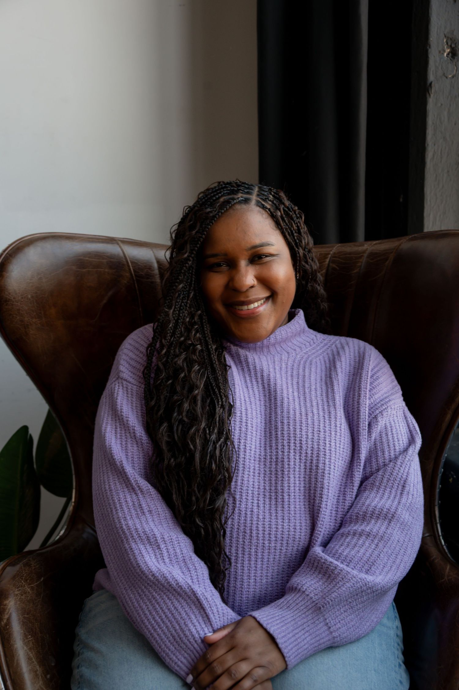 Person in purple sweater relaxing on brown leather chair with natural lighting.