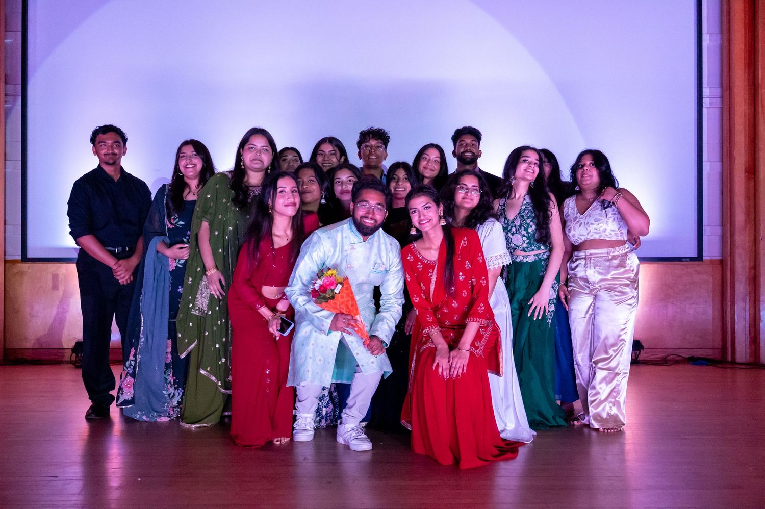 Group photo of performers on stage with purple backdrop lighting.