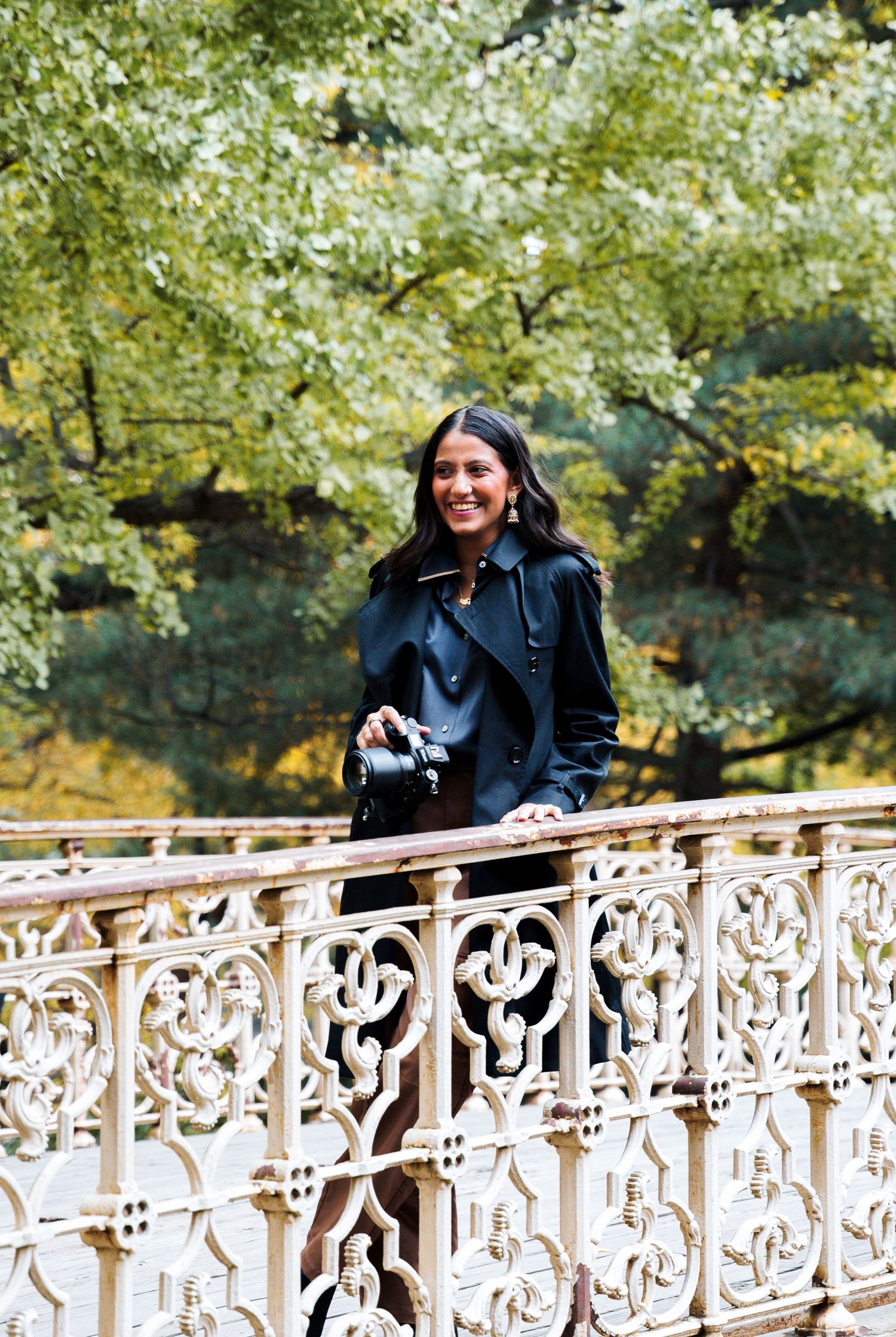 Outdoor portrait on an ornate white bridge surrounded by lush green foliage.