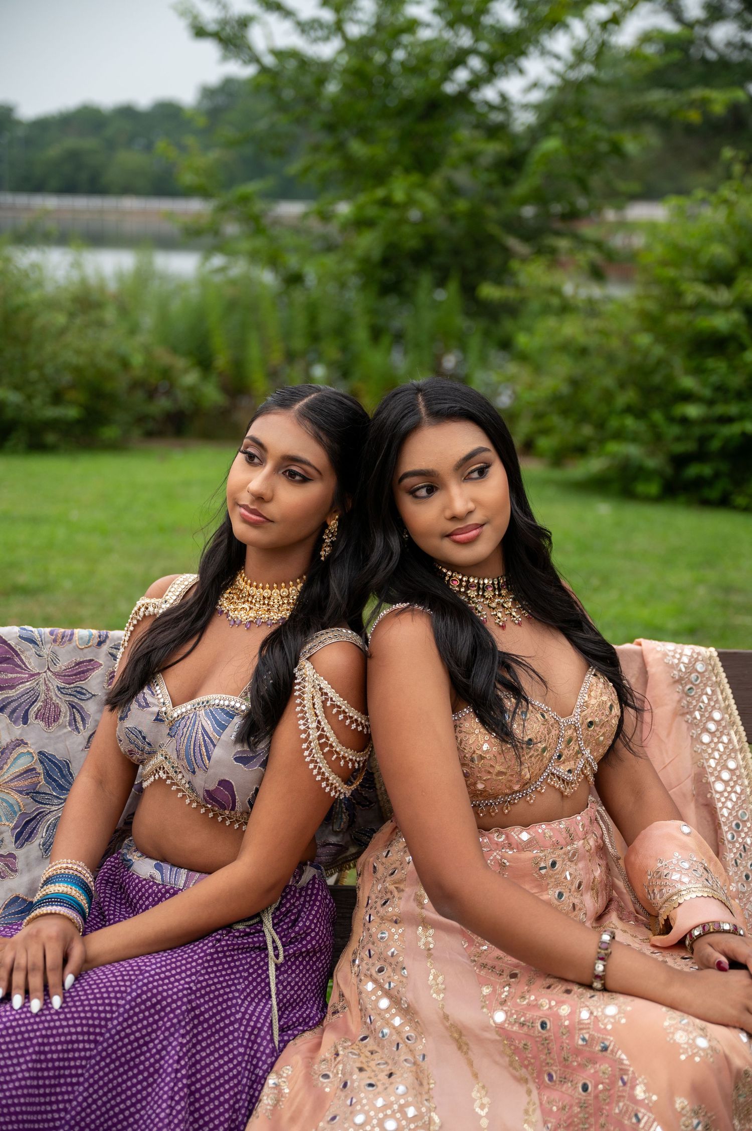 Models in complementary purple and peach formal dresses pose together outdoors.