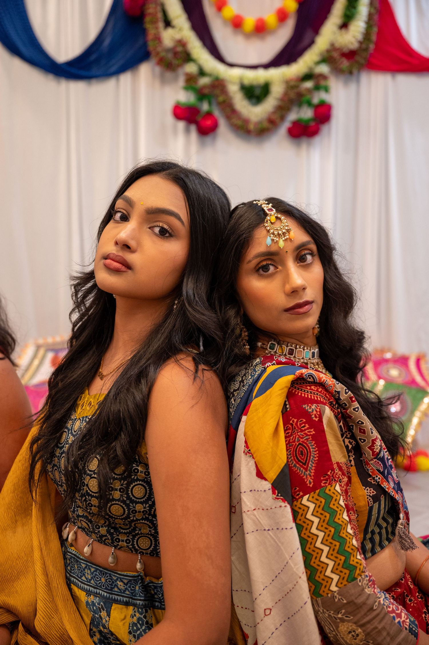 Women in colorful traditional Indian outfits posing against festive decorated backdrop.