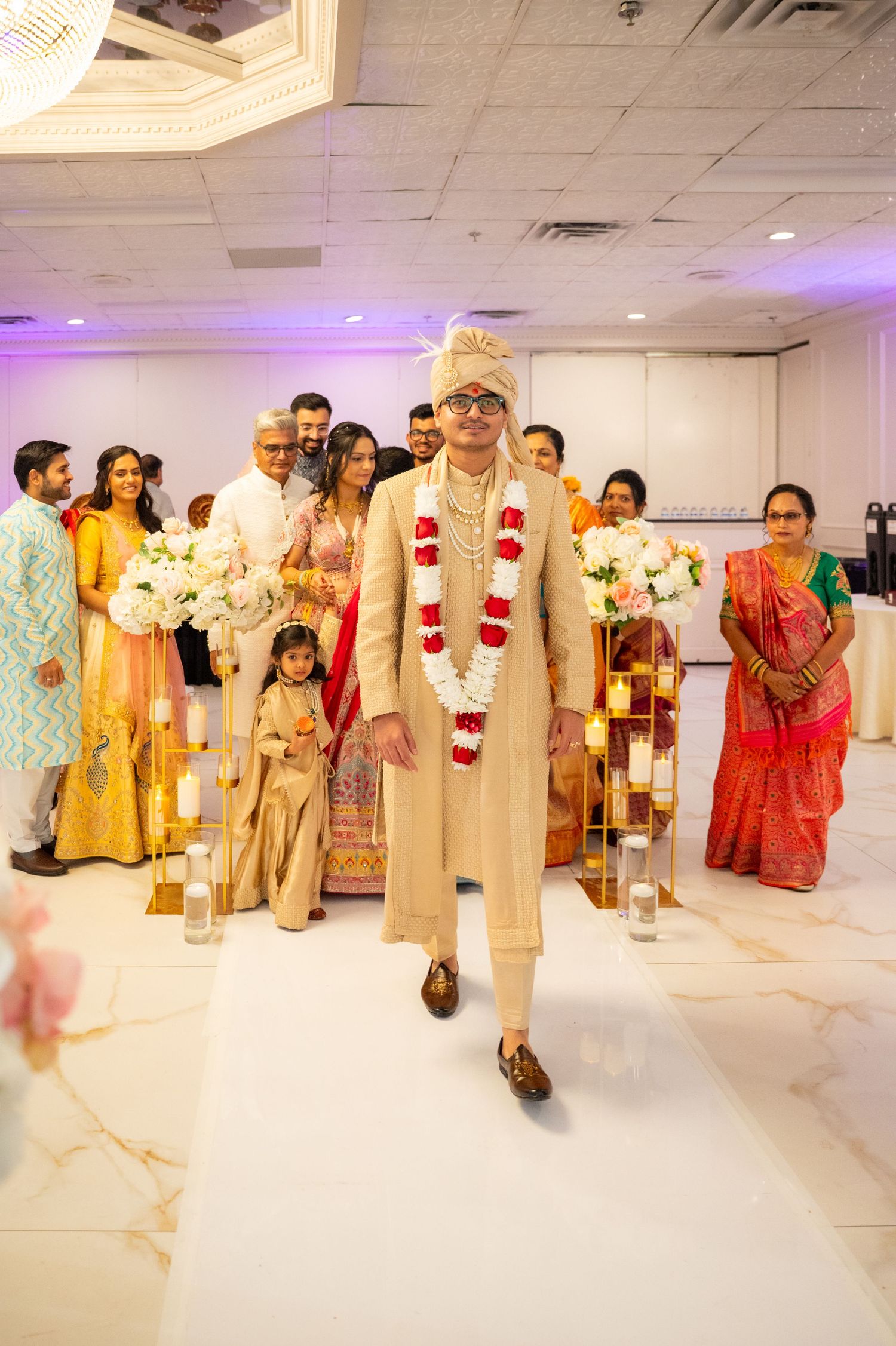 Wedding party members in traditional Indian clothing walking on a white indoor runway.