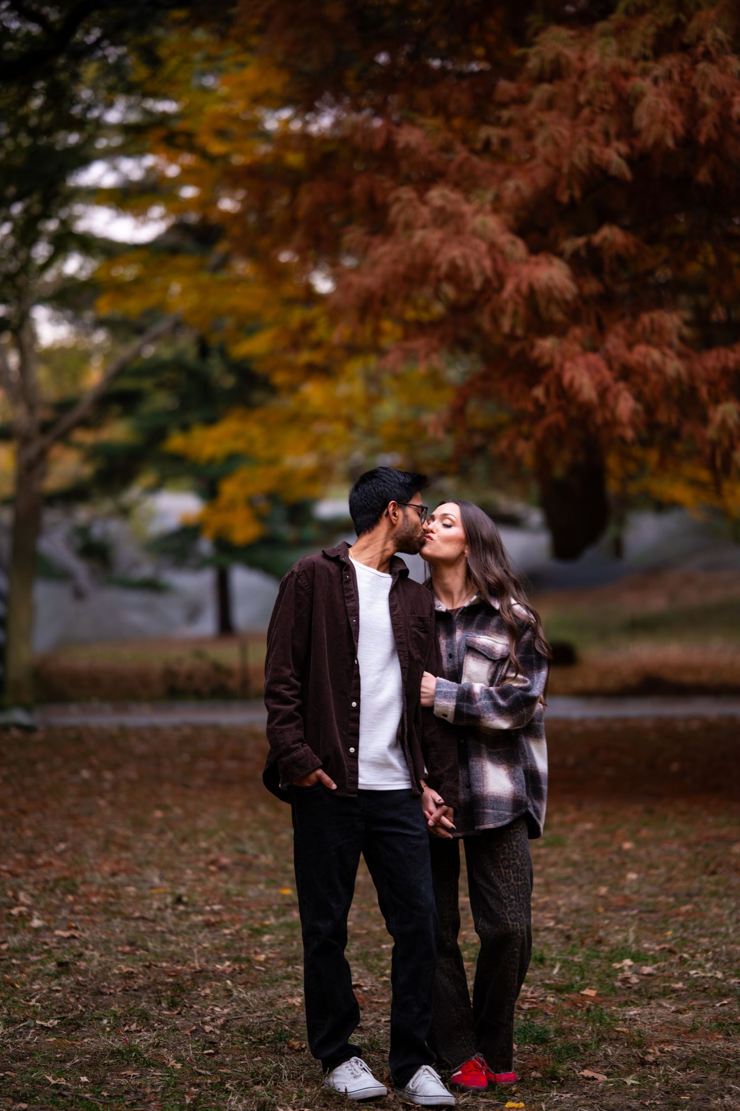A couple shares an intimate moment among fall foliage in a park setting.