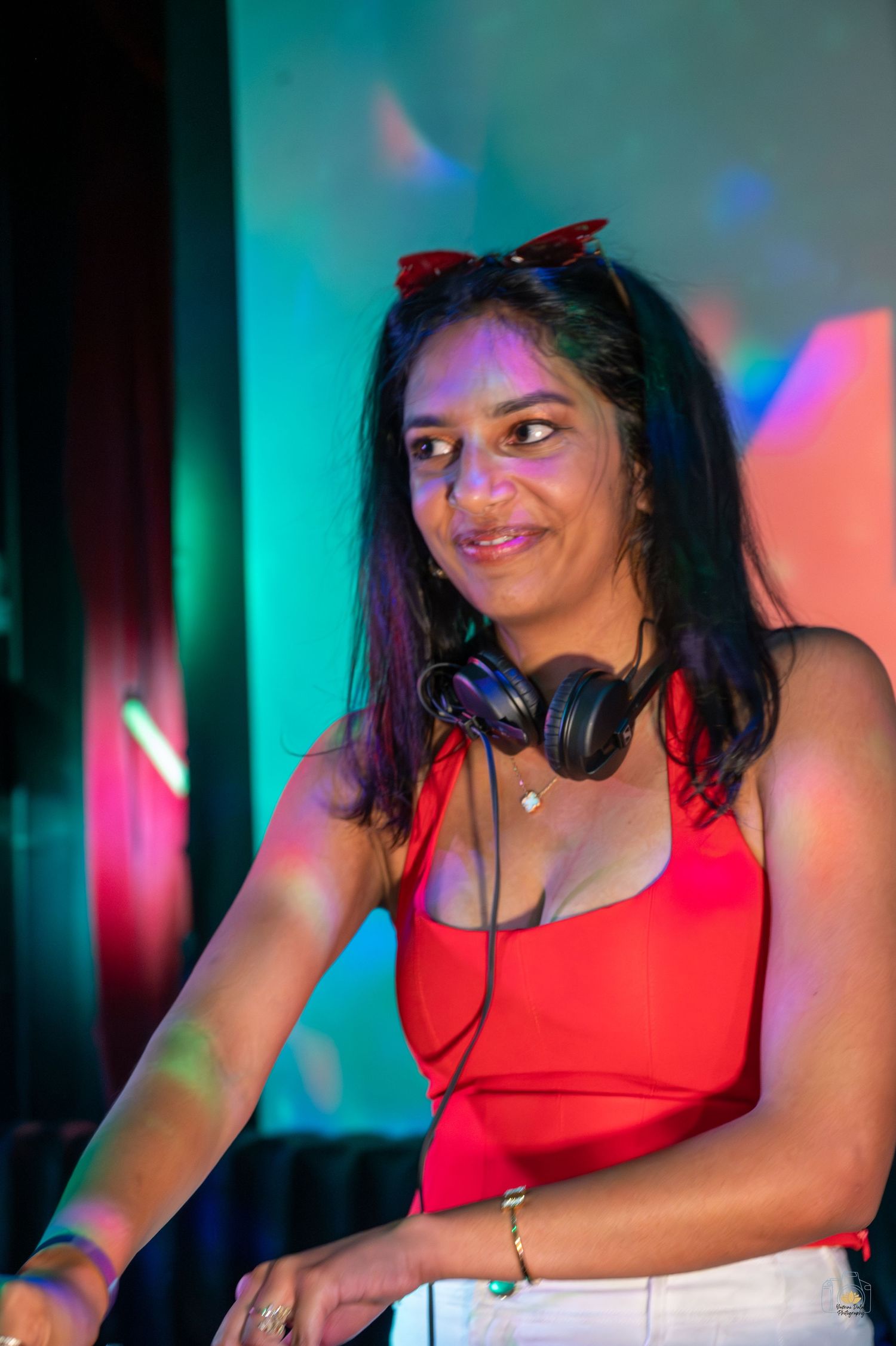 Person in red top dancing under colorful club lighting.