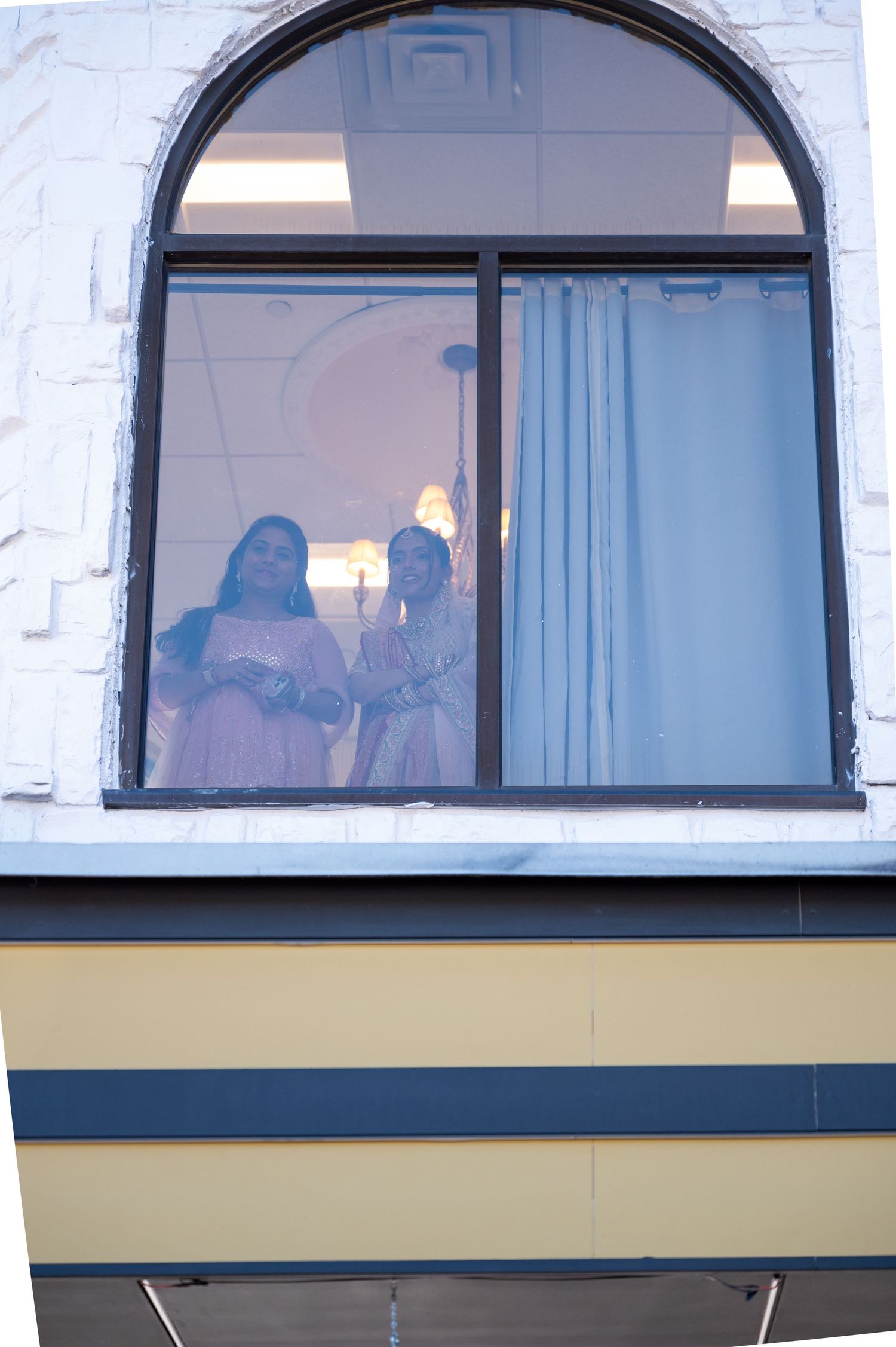 bride watching from arched windows during an indoor celebration.
