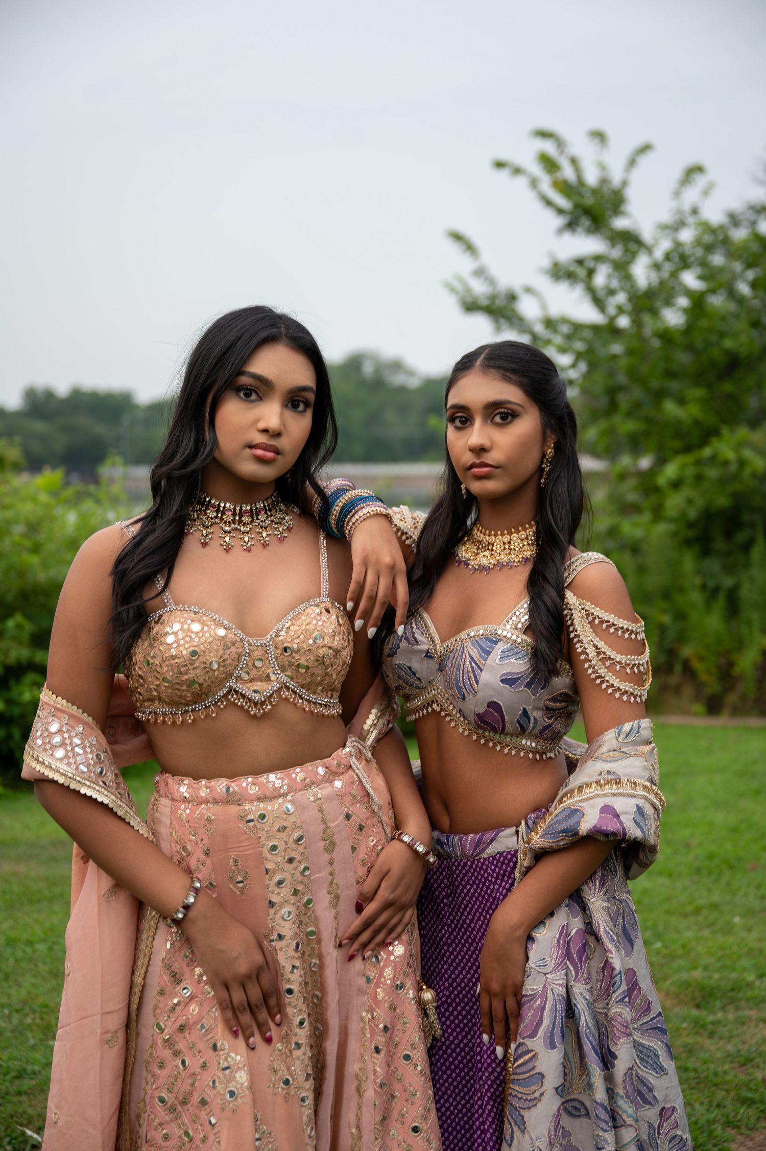Models wearing traditional South Asian formal wear pose together in outdoor setting.