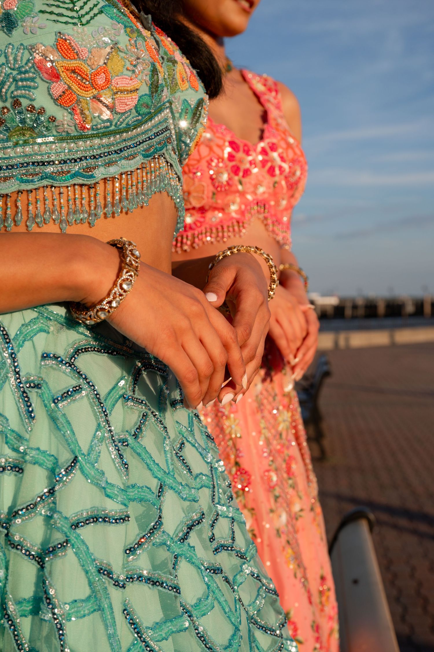 Two people wearing vibrant coral and mint green sequined dresses pose together outdoors.