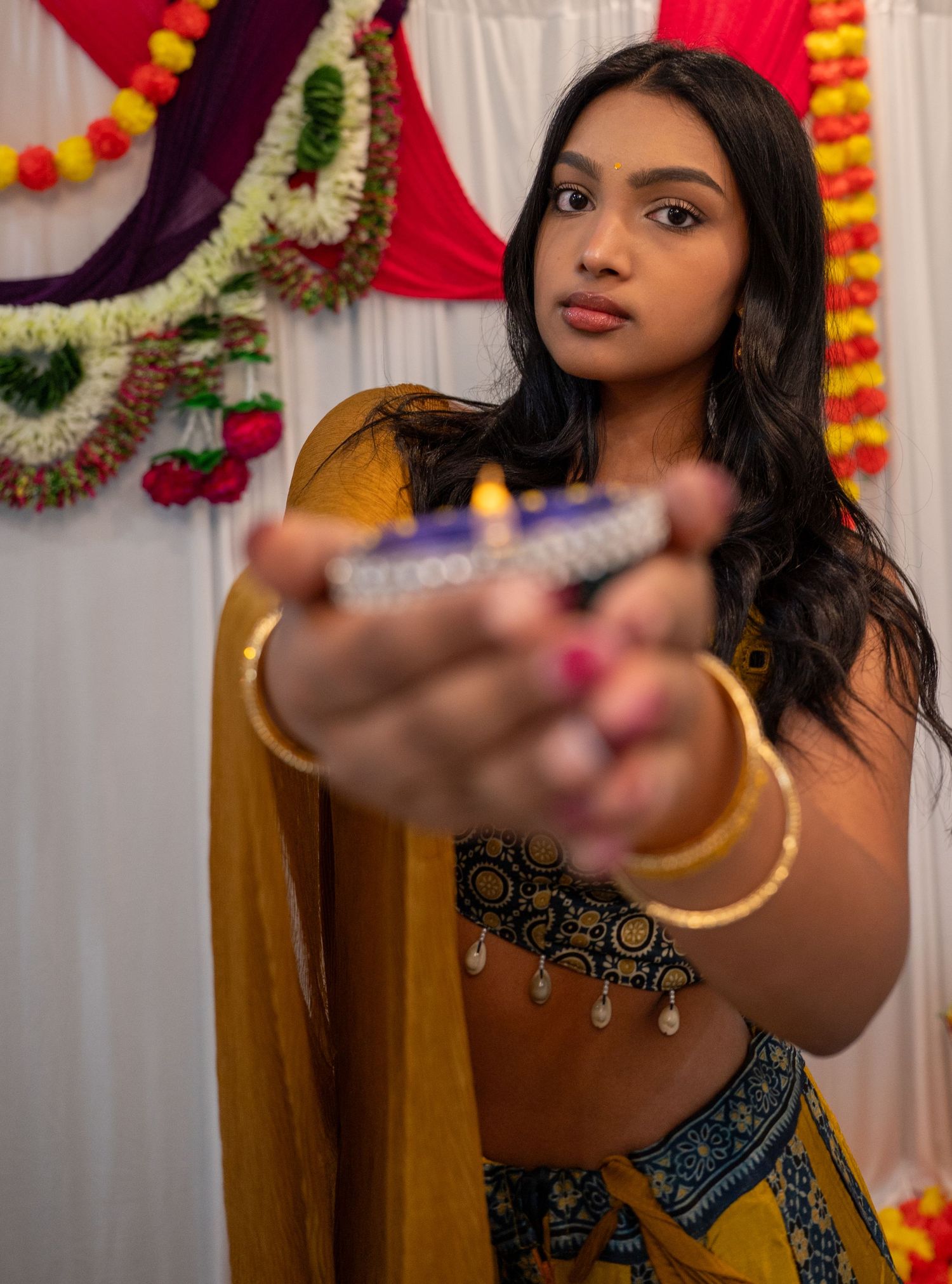 Woman in traditional Indian attire with jewelry posing against colorful decorated backdrop.