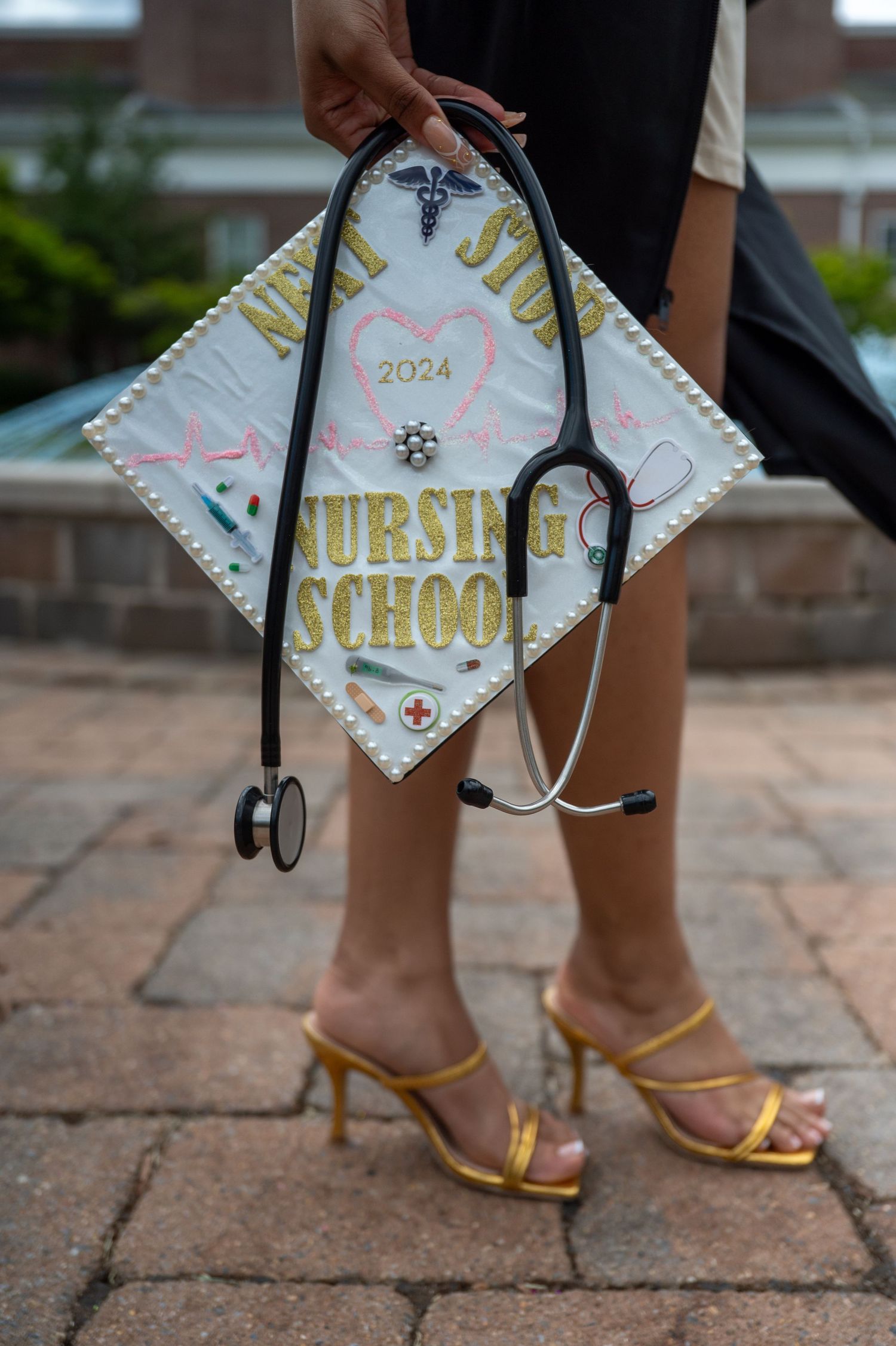 A decorated graduation cap with gold lettering and medical symbols on a brick surface.