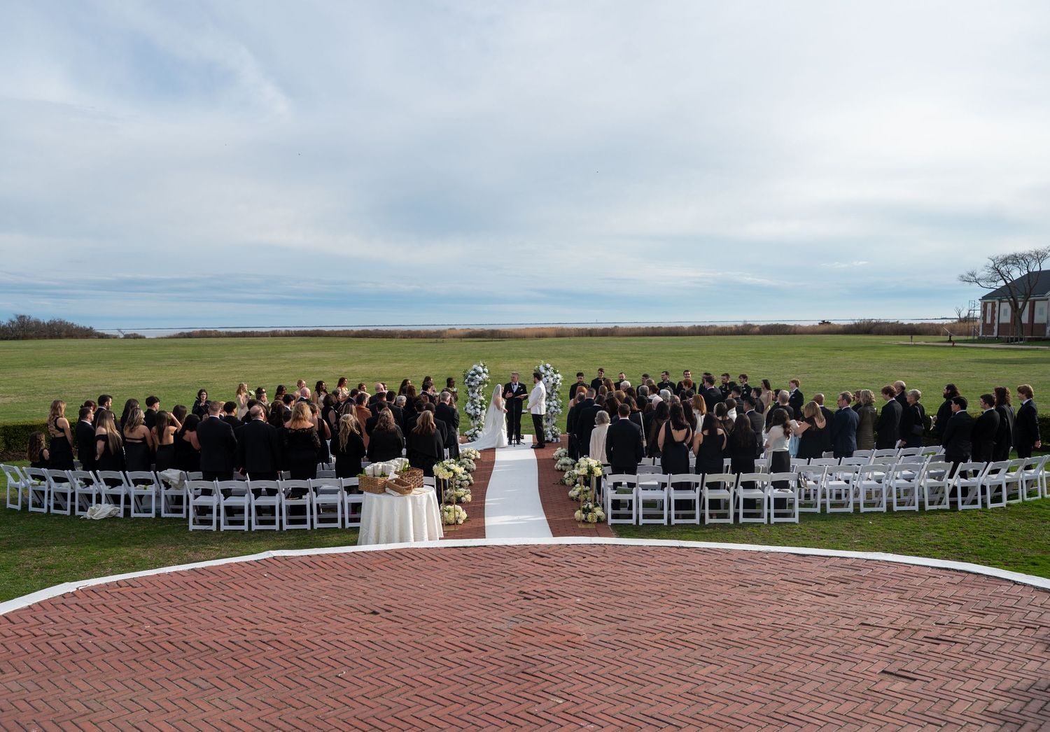 Panoramic view of an outdoor wedding ceremony setup with white chairs on a grassy lawn against a scenic backdrop.