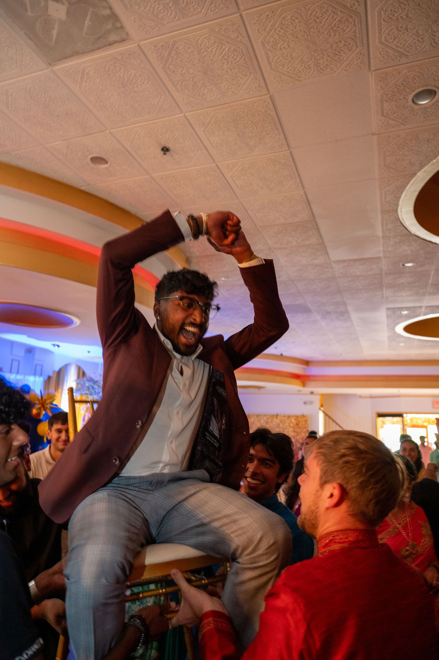 Person in burgundy jacket being lifted up by crowd during celebratory event.