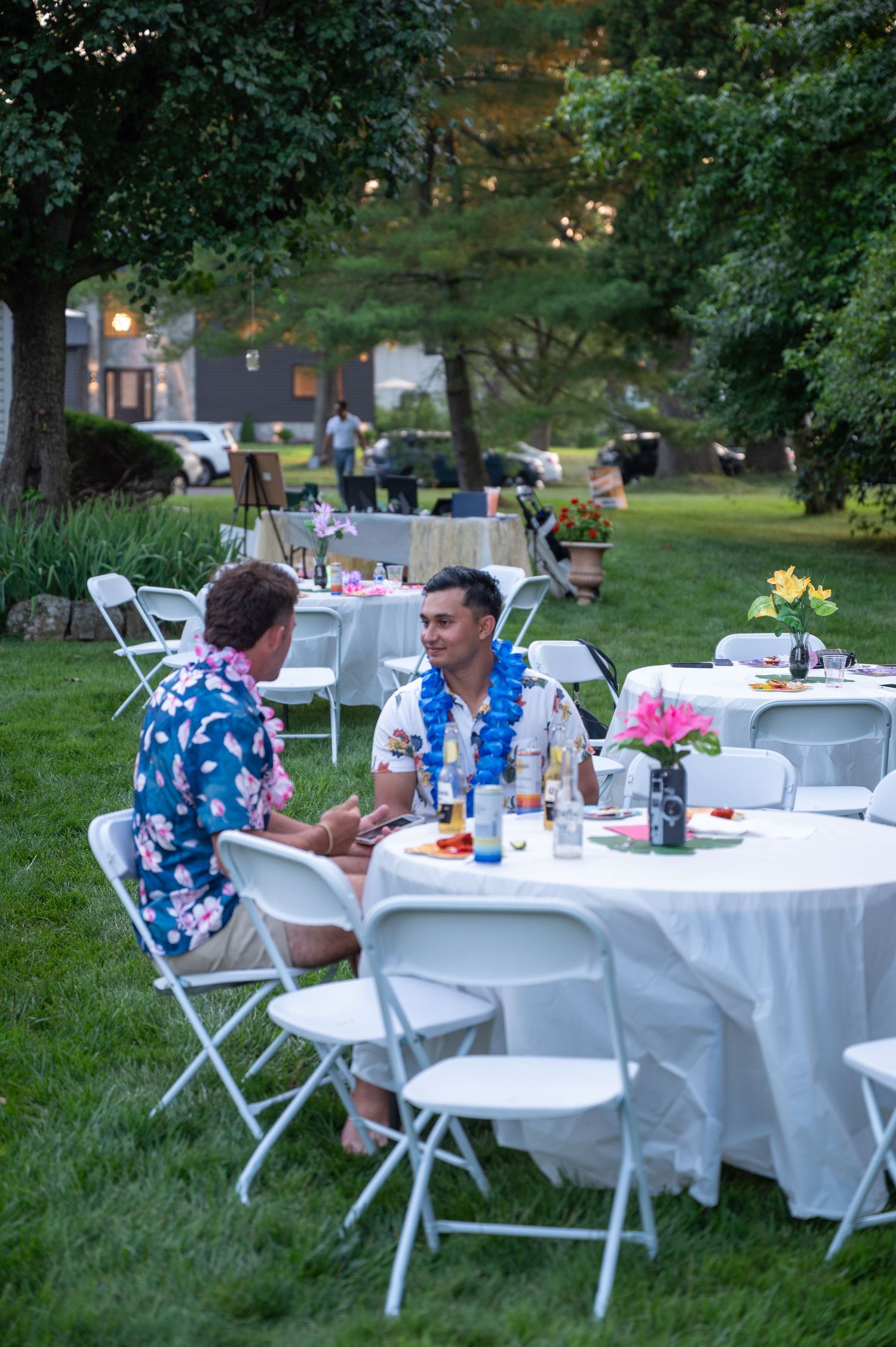Outdoor graduation party setup with white tables and chairs arranged on a grassy lawn.