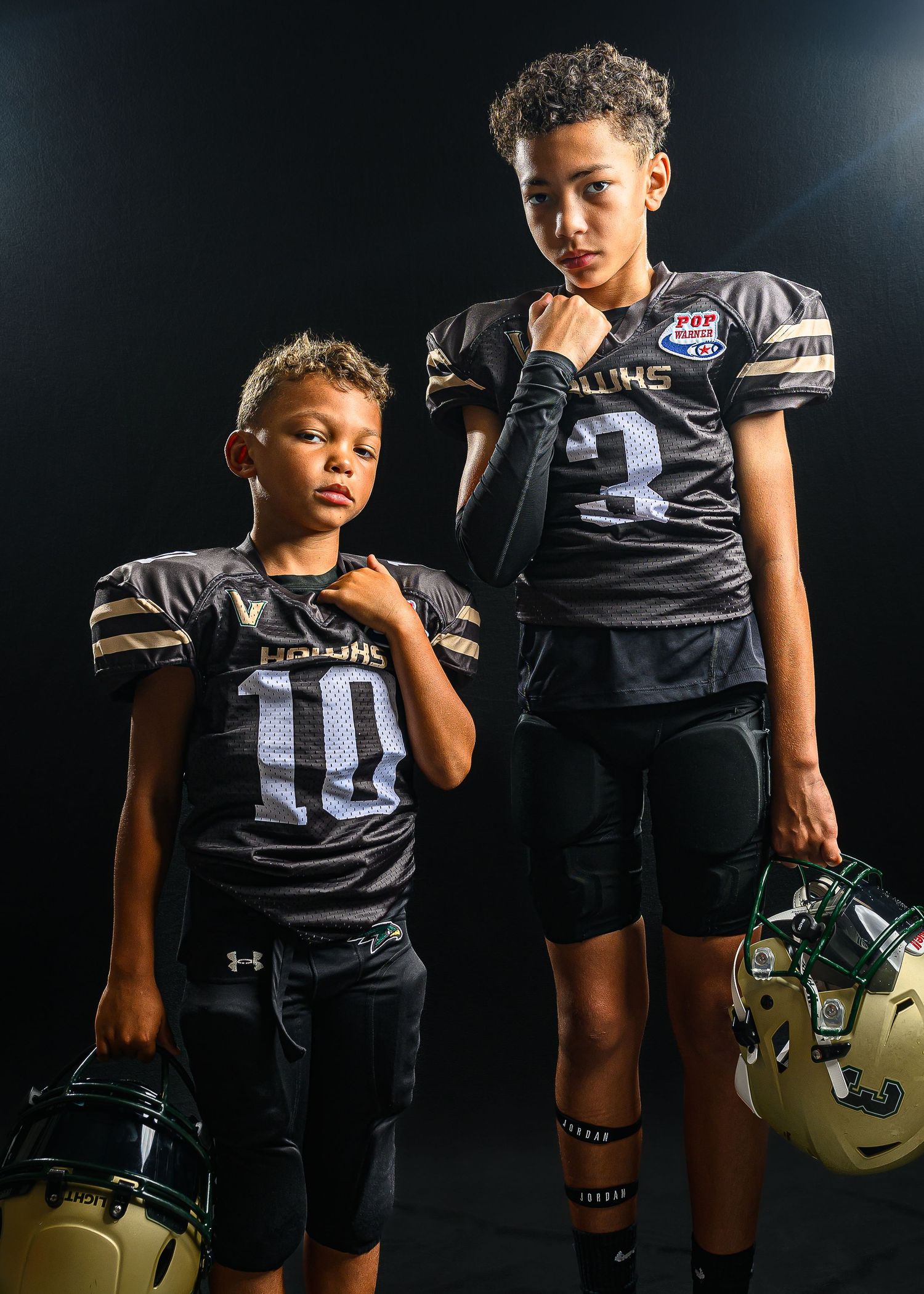Football player in black uniform and gold helmet stands against dark background in striking moody portrait series.