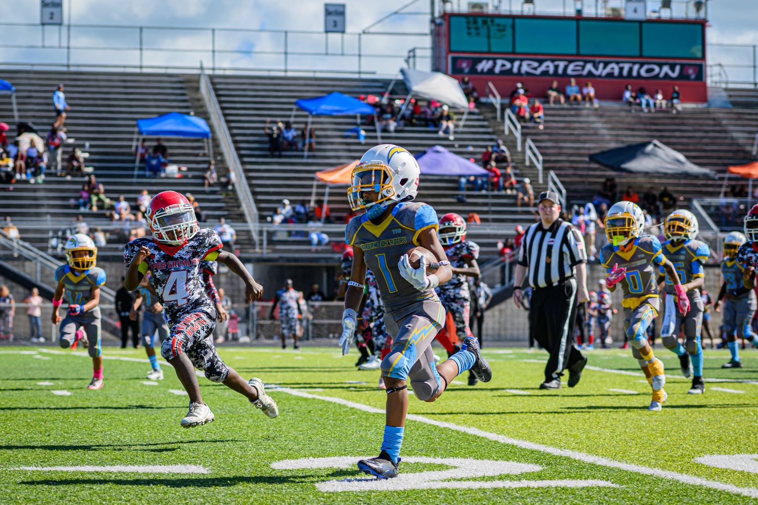 Football players in action during a youth game at a stadium with spectators in bleachers.