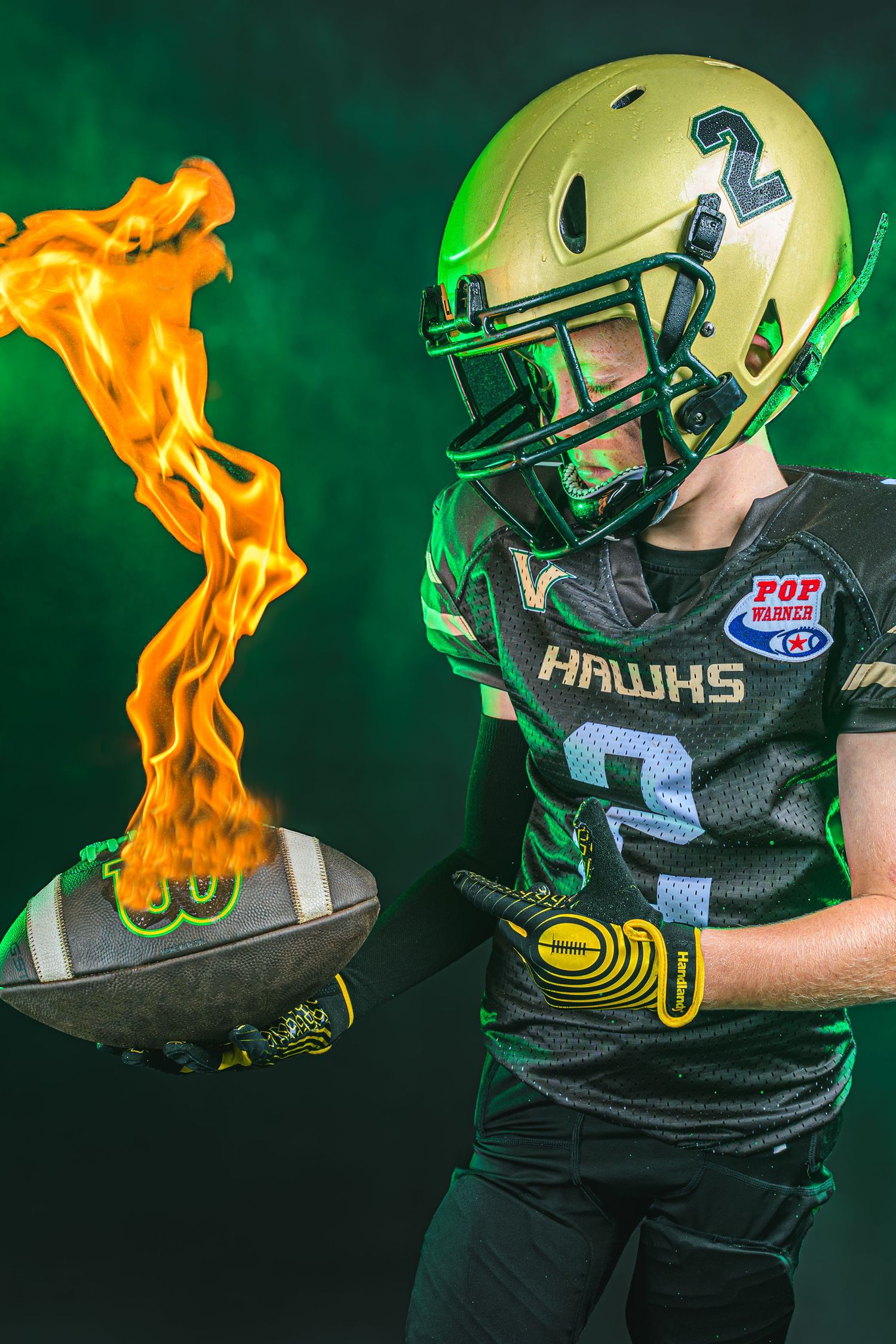 Youth football player in black and green uniform stands next to flaming football in dramatic sports photograph.